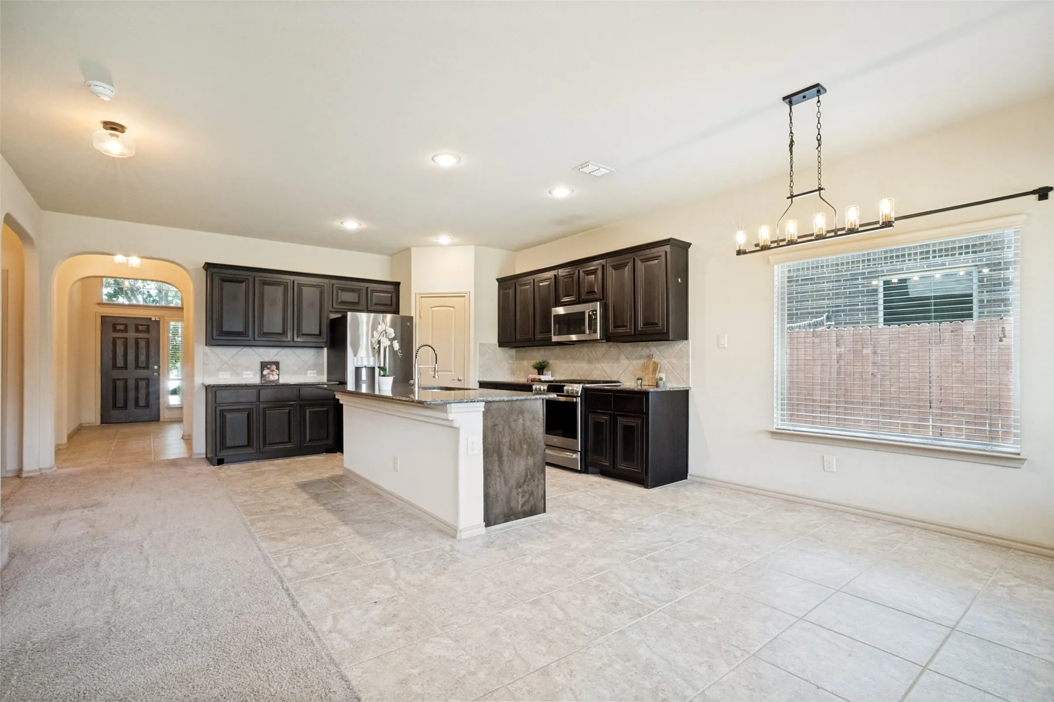 Open-concept kitchen and dining area featuring dark wood cabinetry, stainless steel appliances, a center island with bar seating, tile flooring, and an adjacent arched entryway