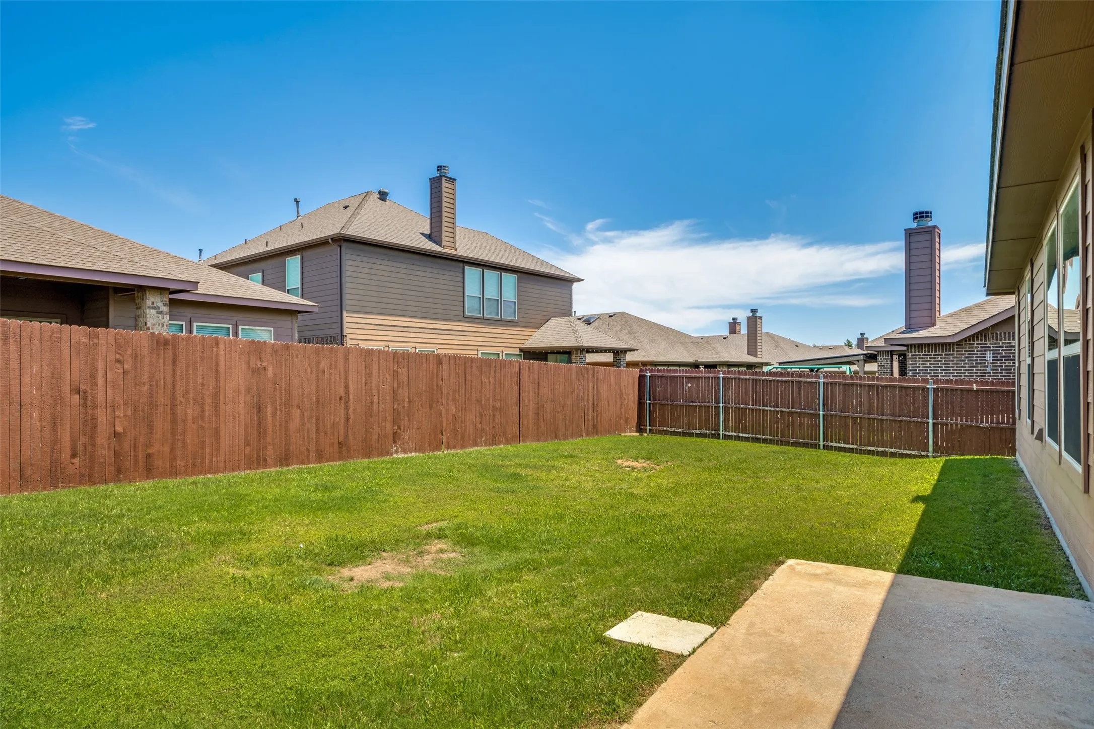 Expansive backyard featuring a manicured lawn, a concrete patio, and a wood privacy fence
