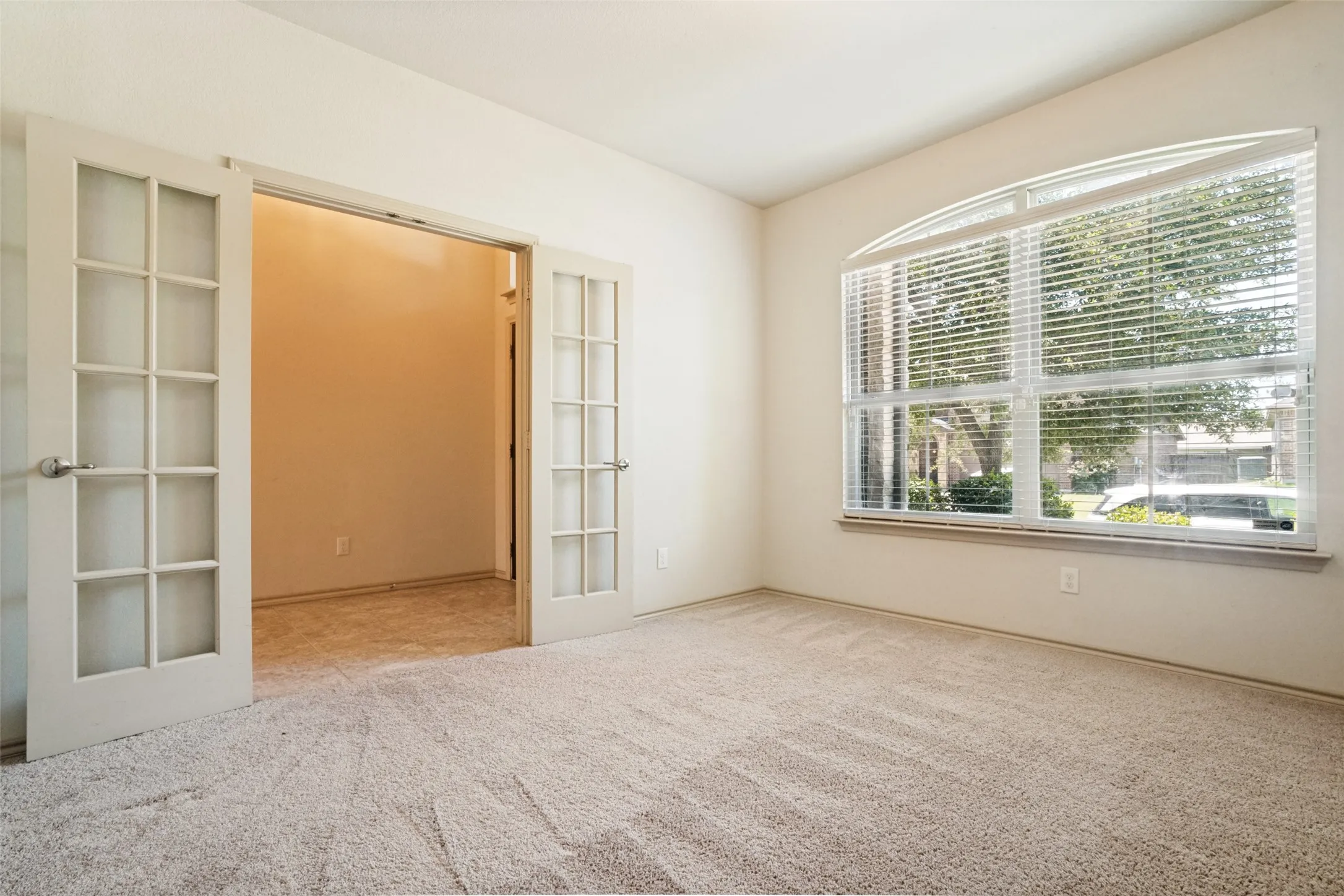 Front office/flex space featuring light-colored carpeting, an arched window with horizontal blinds, and French doors