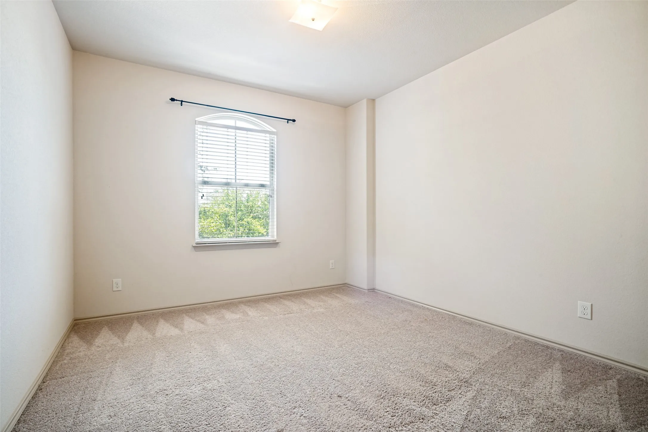 Neutral wall paint throughout this room, featuring light-colored carpet flooring and a single arched window with blinds