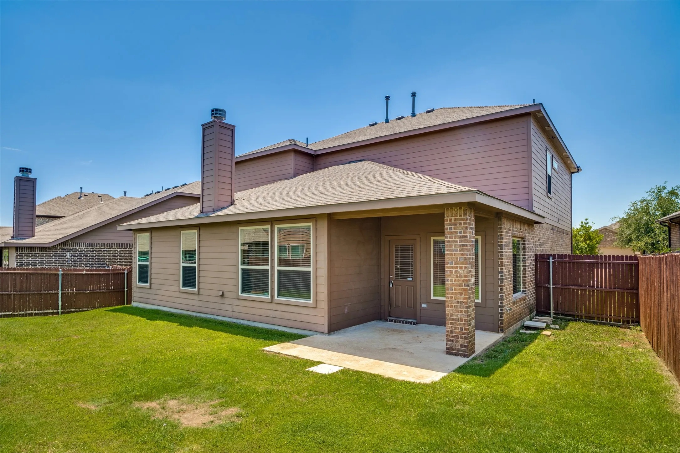 Expansive backyard featuring a concrete patio, brick columns, and a full wooden privacy fence
