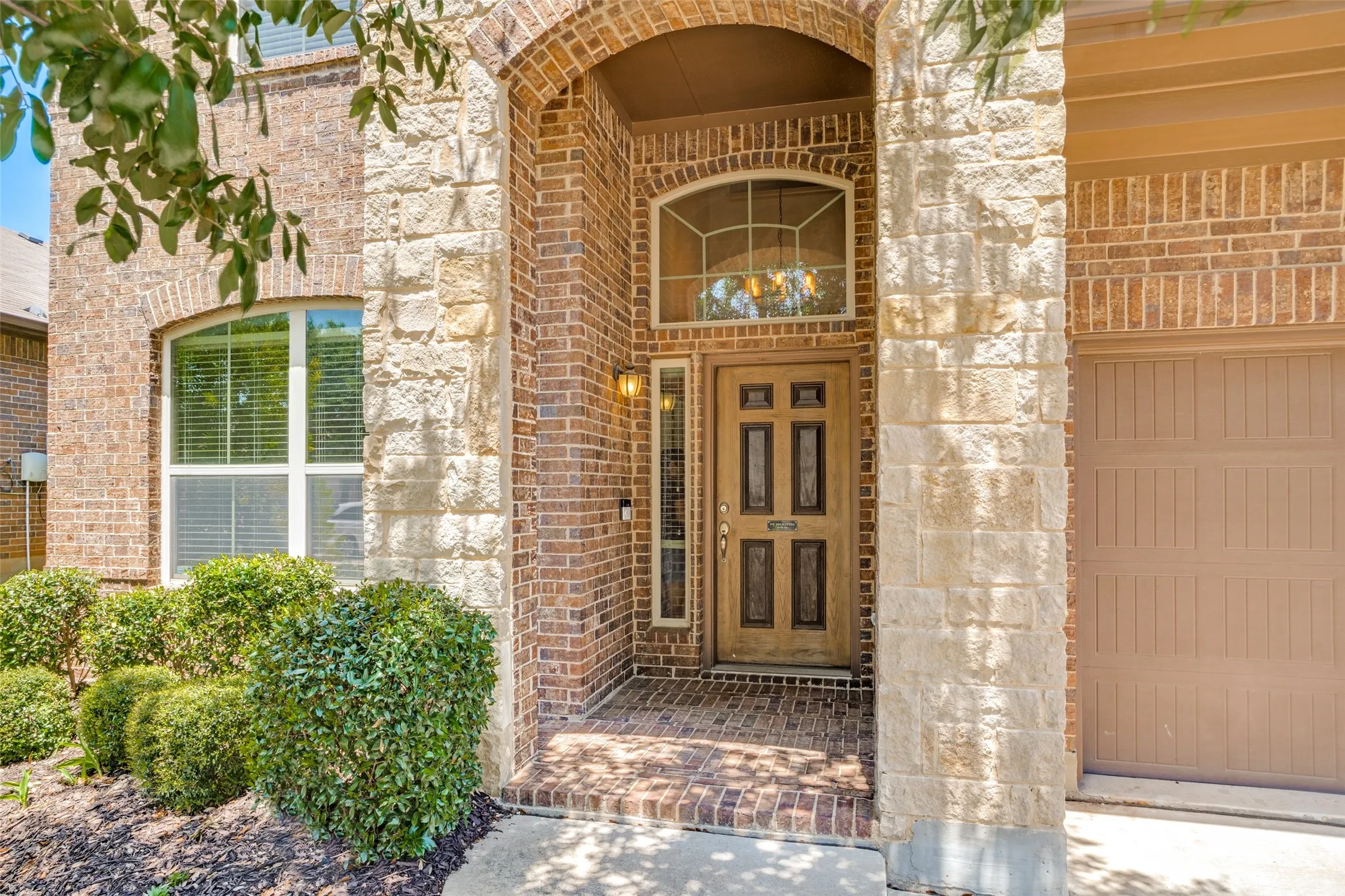 Arched entry with a paneled wood-finish door, brick pavers, mixed brick and stone facade, and an attached garage
