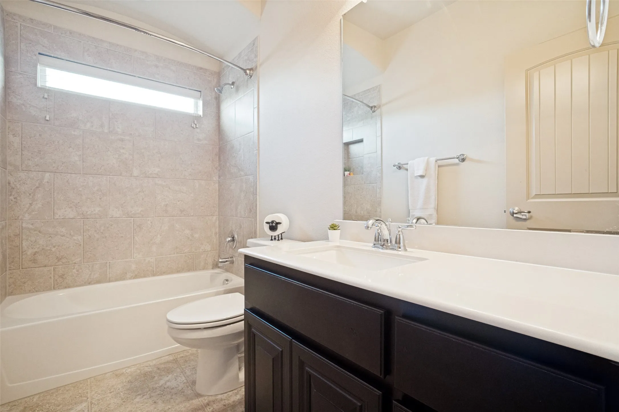 Bathroom featuring a white tub, light-toned wall tiling, and a window above the tub