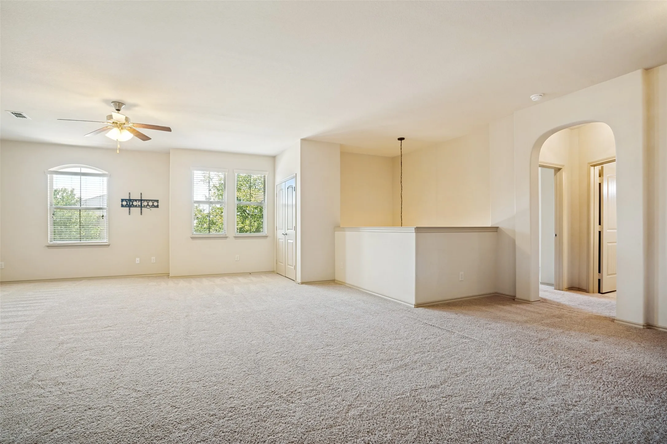 Spacious loft area featuring light-toned carpeting, multiple windows, a ceiling fan, and an arched doorway