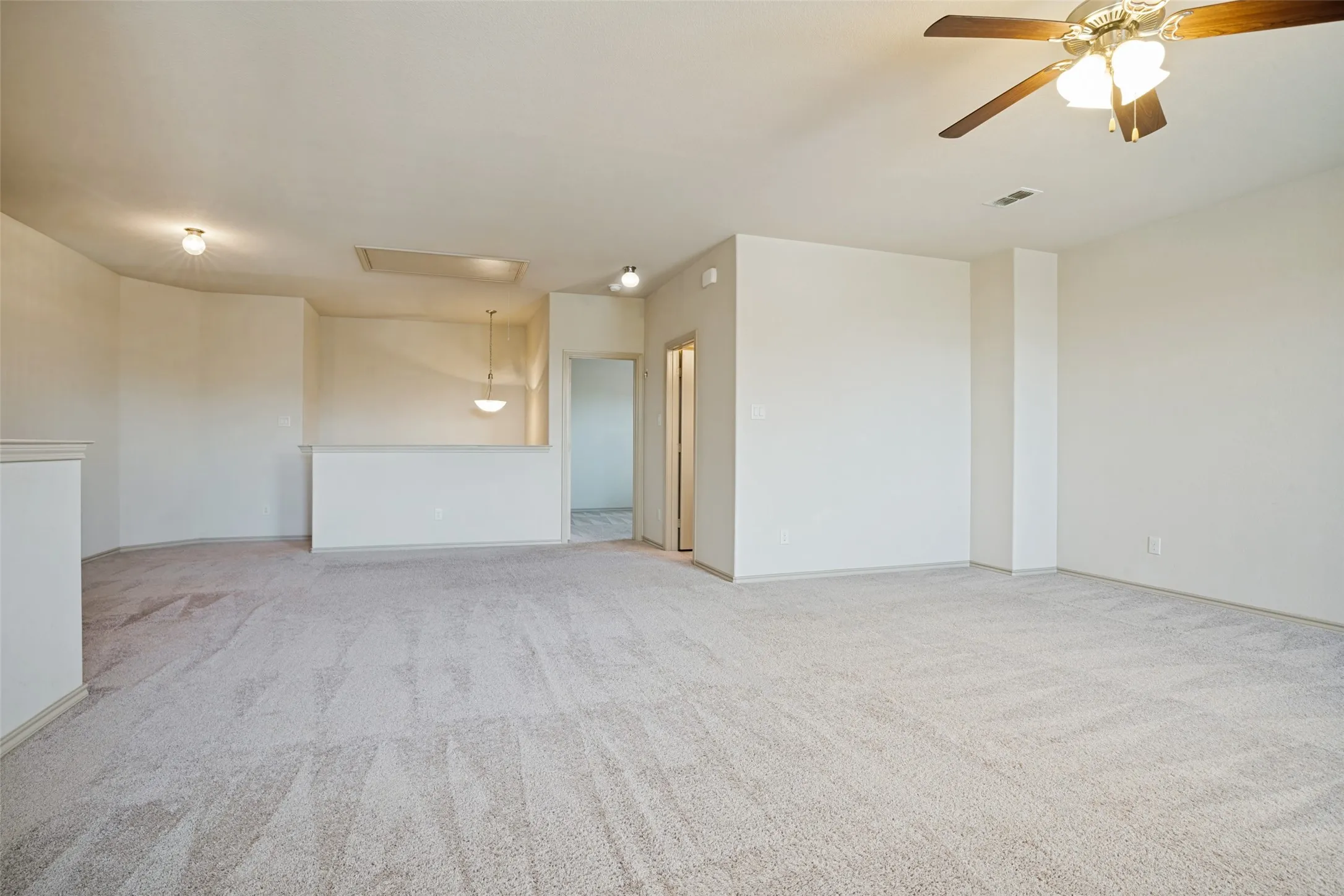 Spacious room featuring light-toned carpet flooring, a ceiling fan with integrated lighting, and multiple recessed light fixtures