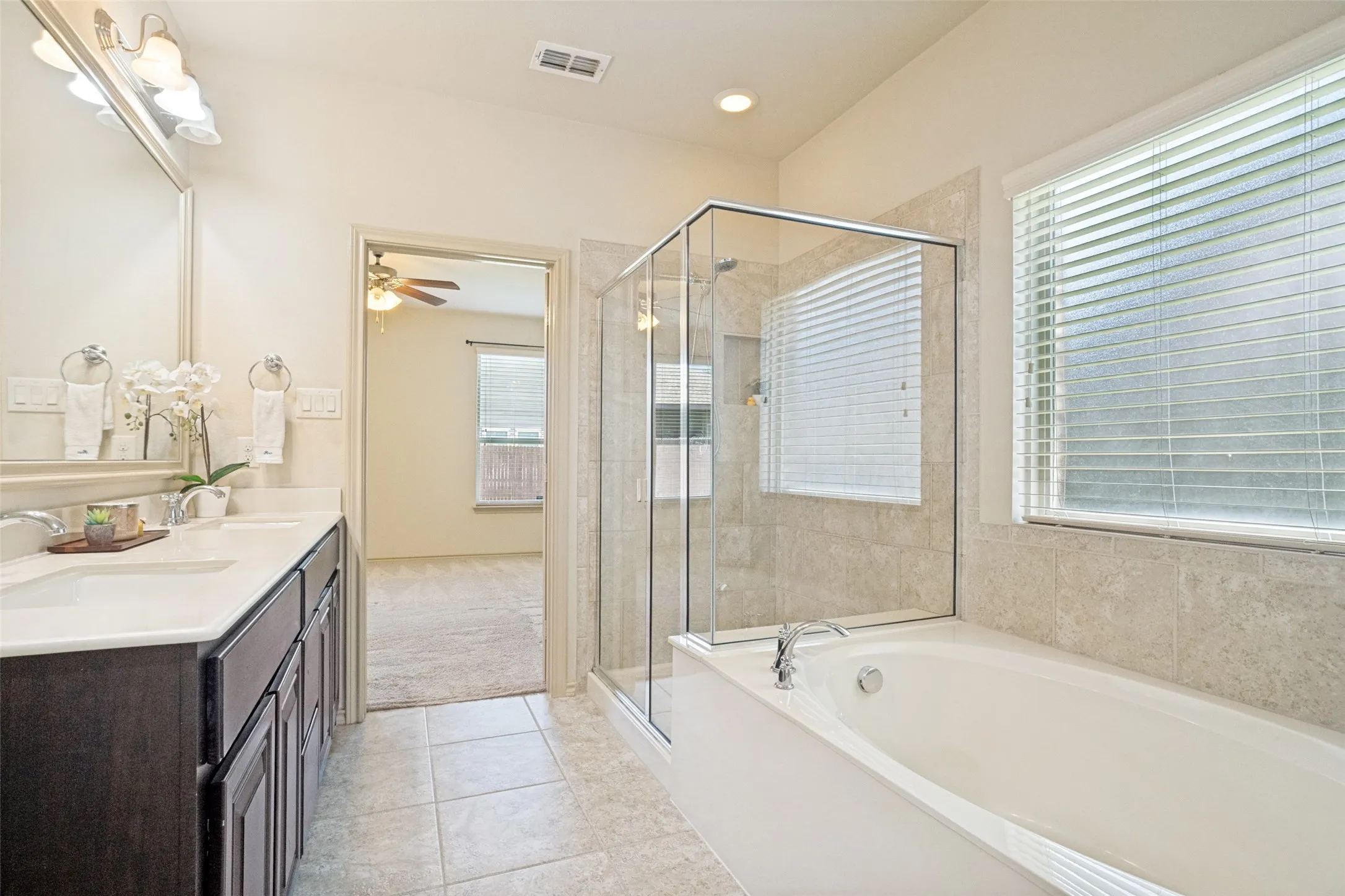 Bathroom featuring a double vanity with ample storage, a glass-enclosed shower, a built-in soaking tub, and tile flooring