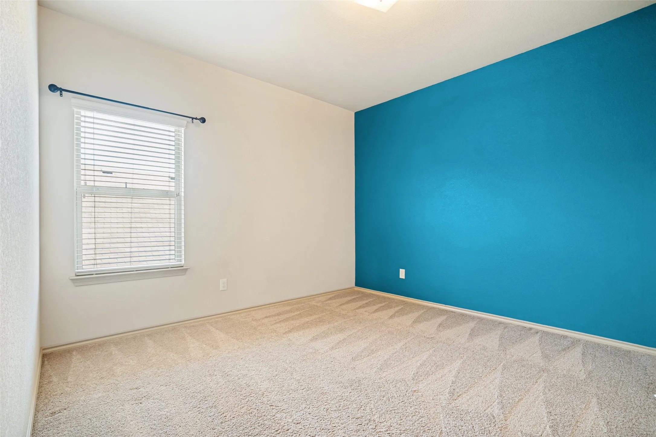 Room featuring light-colored carpet, a window with horizontal blinds, and a contrasting accent wall