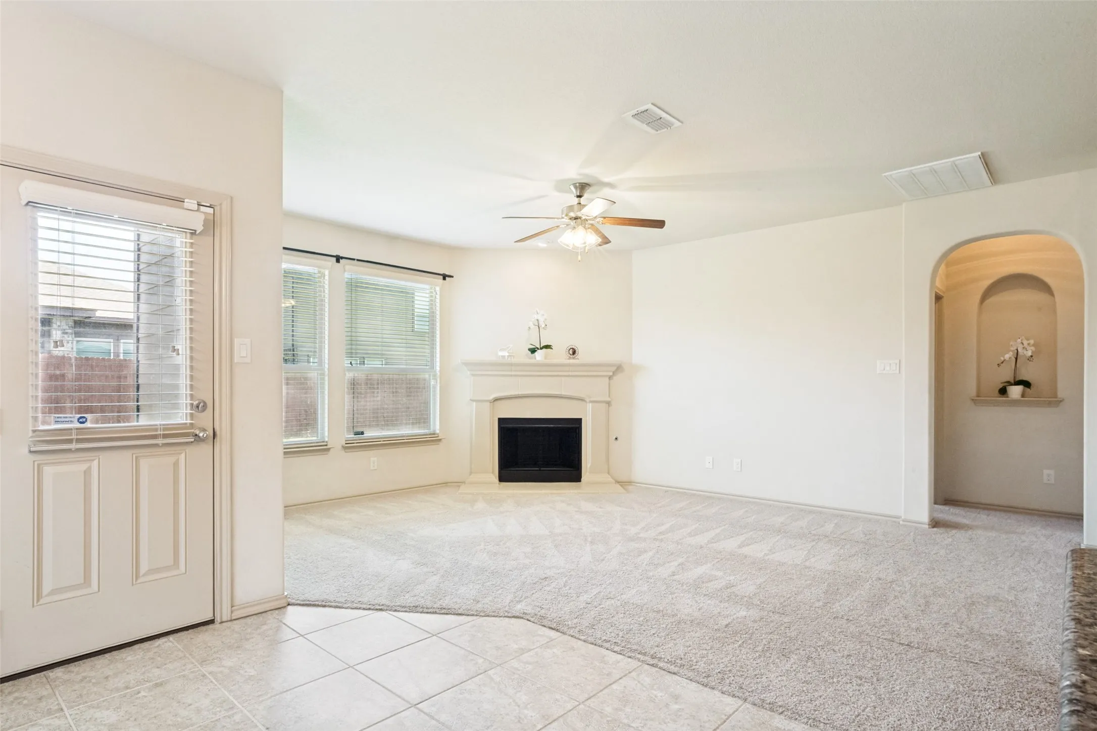 Spacious living area featuring a fireplace with a decorative mantel, multiple windows with blinds, a ceiling fan, an arched entryway, and a built-in display niche