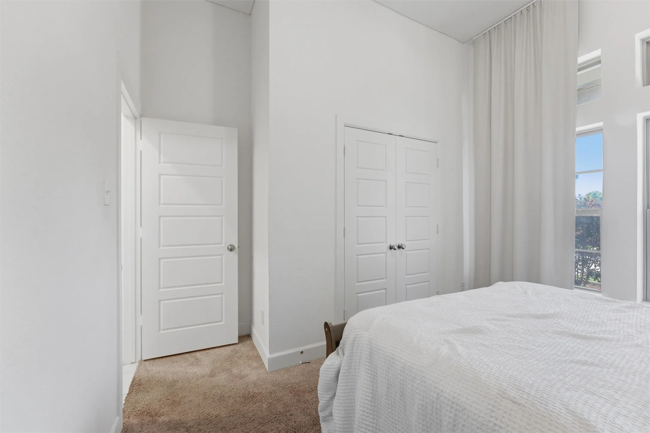 Bright interior space featuring high ceilings, multiple windows, carpet flooring, and white paneled​​‌​​​​‌​​‌‌​‌‌​​​‌‌​‌​‌​‌​​​‌​​ doors