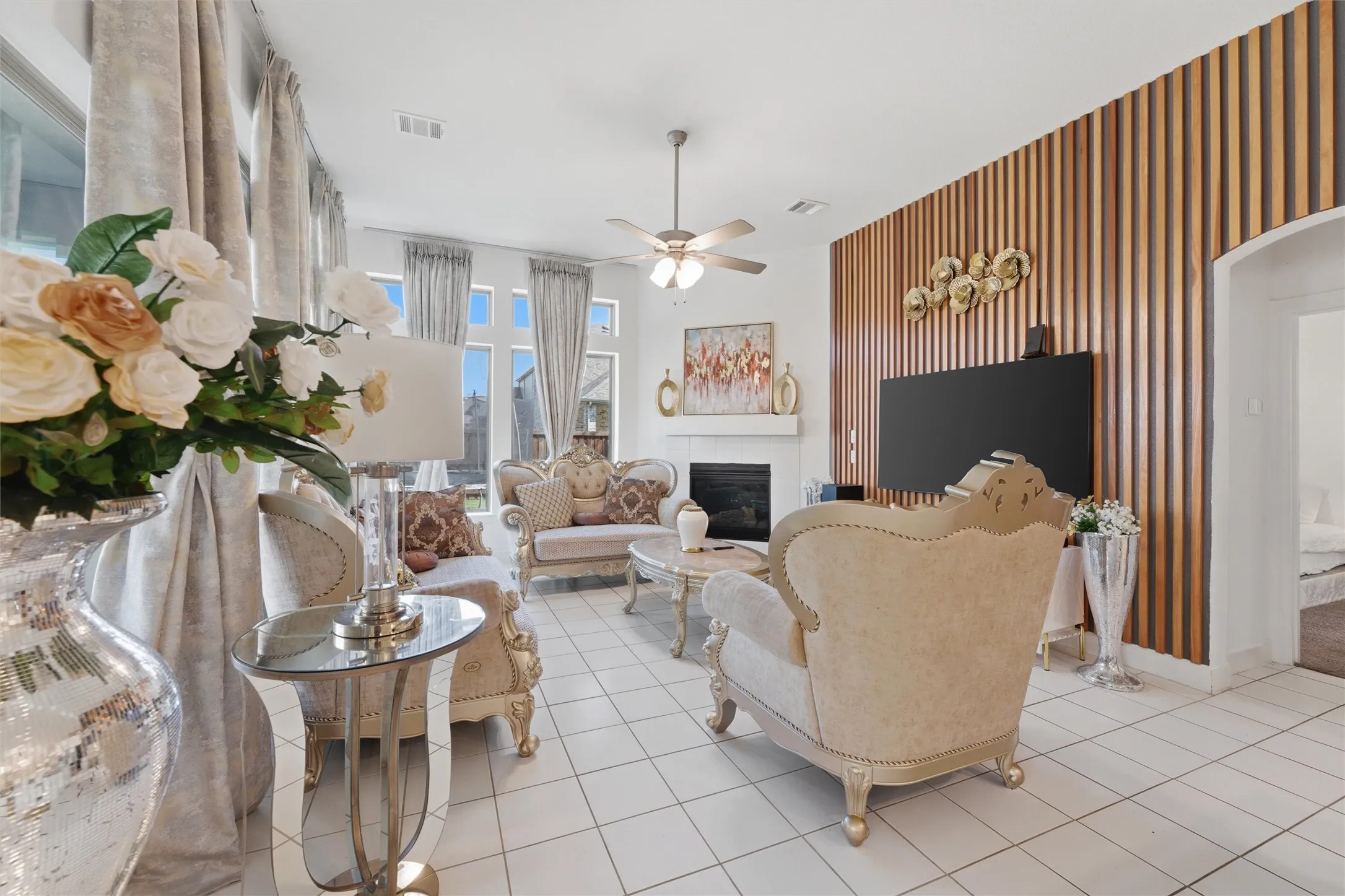 Spacious living area featuring white tile flooring, a fireplace with a white mantel, and a distinctive wood slat accent wall