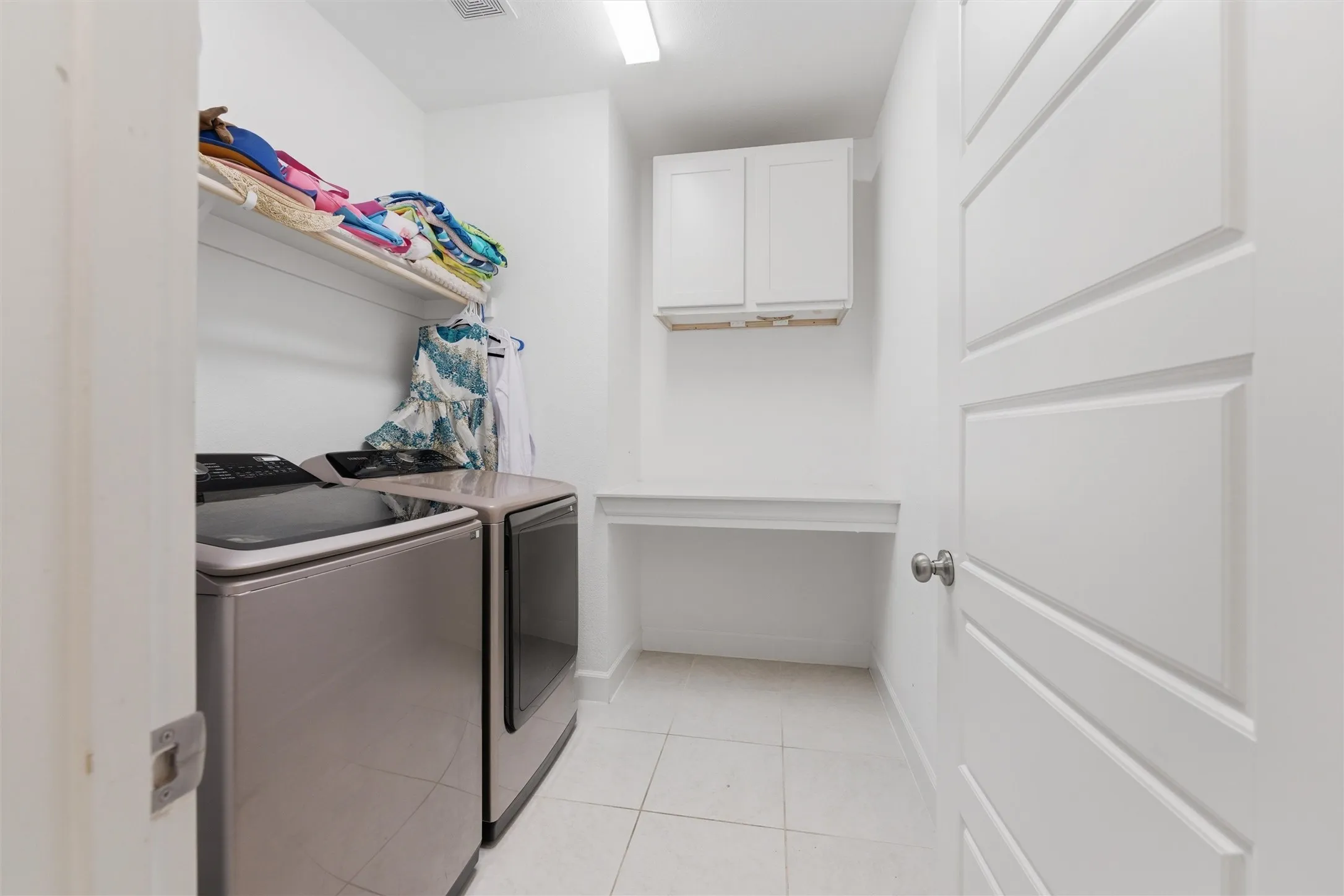 Dedicated laundry area featuring white tile flooring, white shaker-style cabinetry, and a built-in folding counter