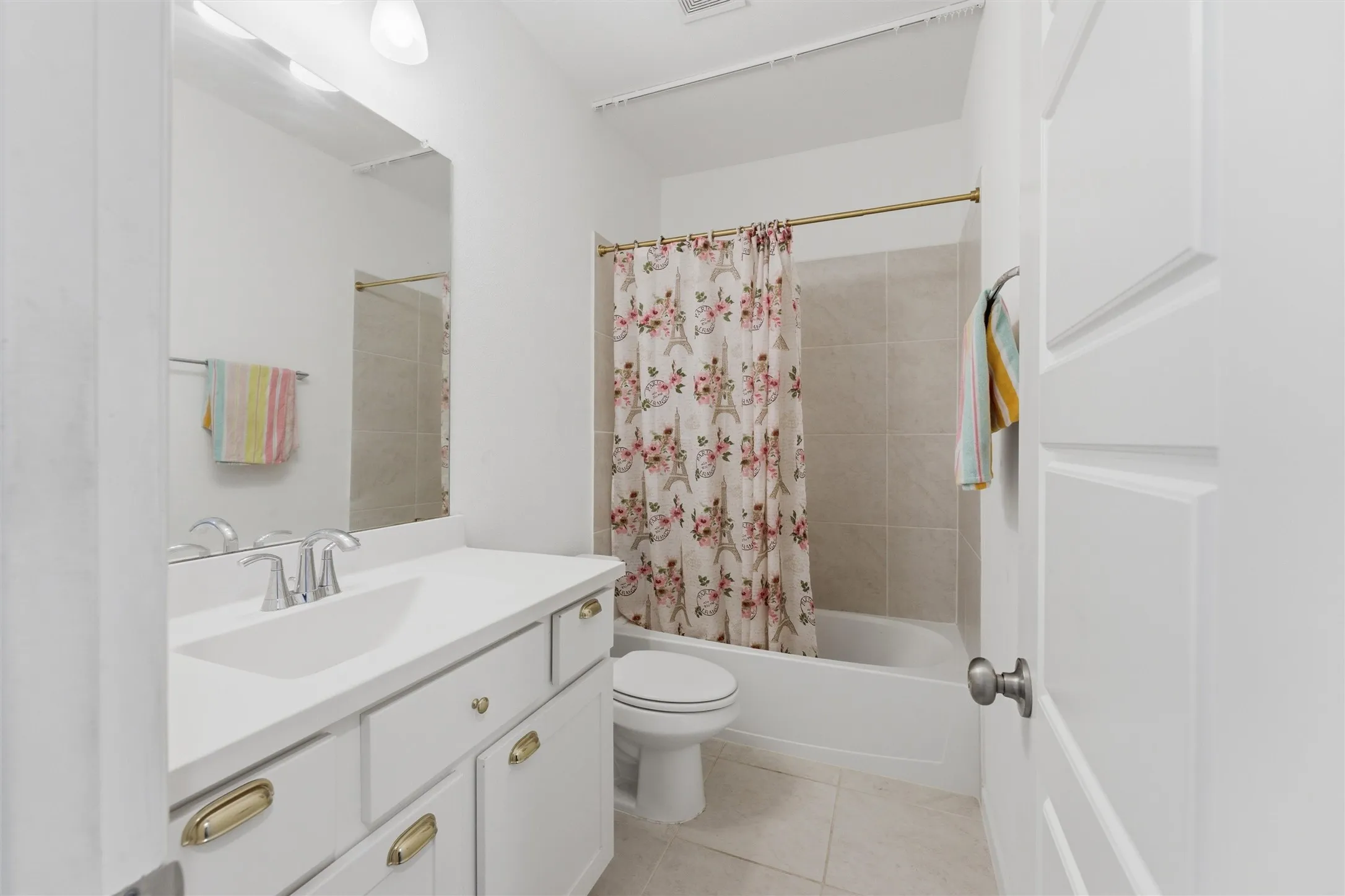 Bathroom featuring a single-sink vanity with white cabinetry and brass hardware, an integrated sink, and a framed mirror