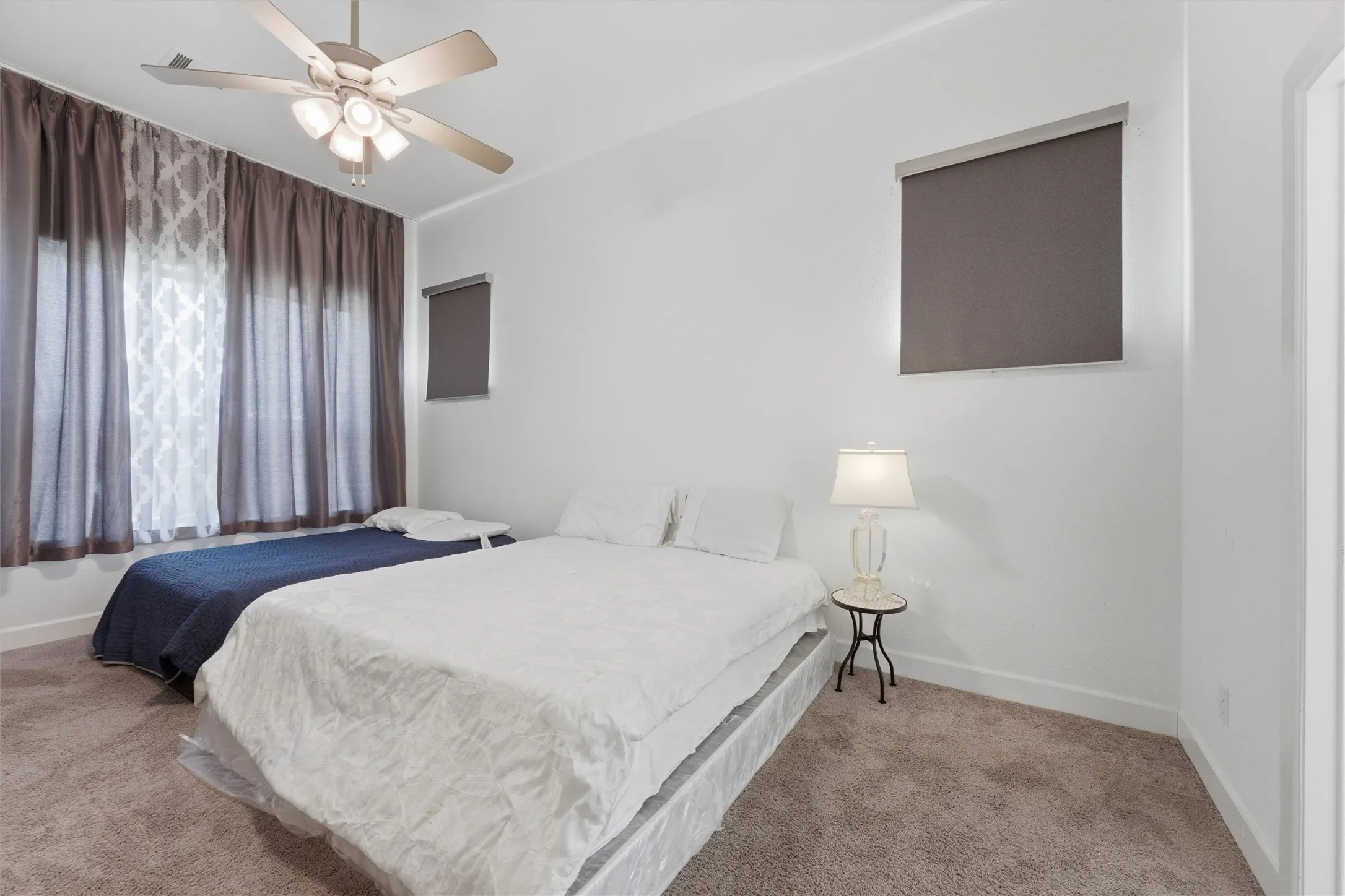 Neutral-toned bedroom featuring a ceiling fan with integrated lighting, wall-to-wall carpeting, and bright white walls
