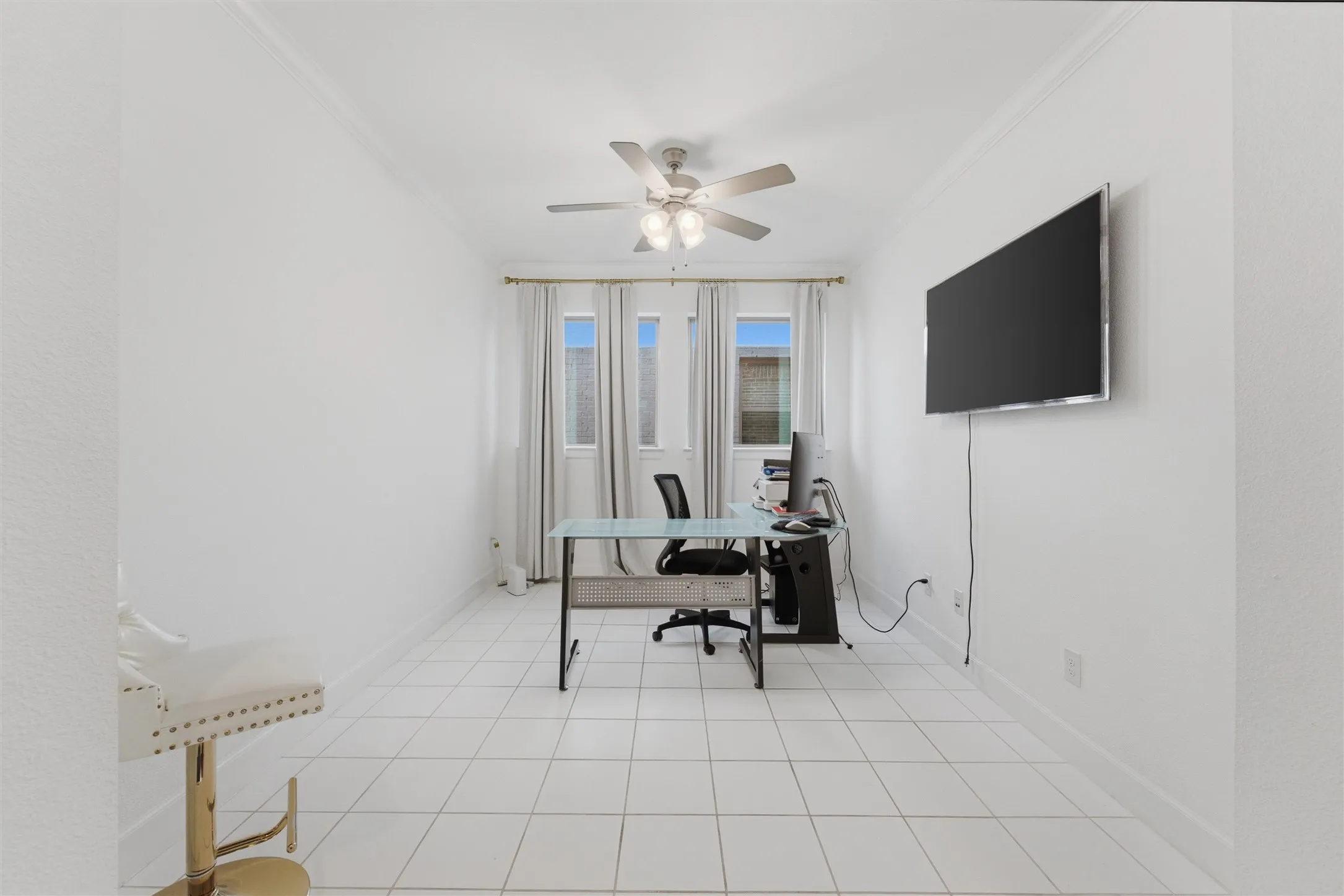 Bright room featuring light-colored tile flooring, multiple windows with curtains, and a ceiling fan with integrated lighting