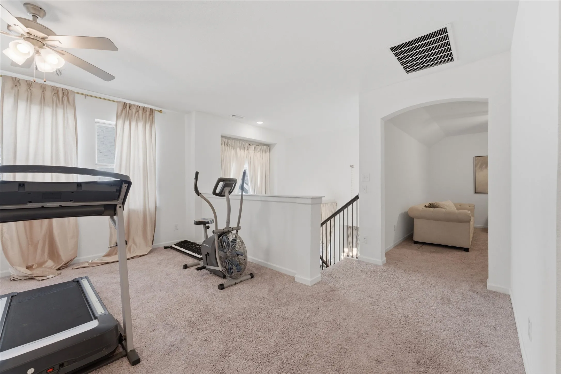 Carpeted open area with white walls and a ceiling fan