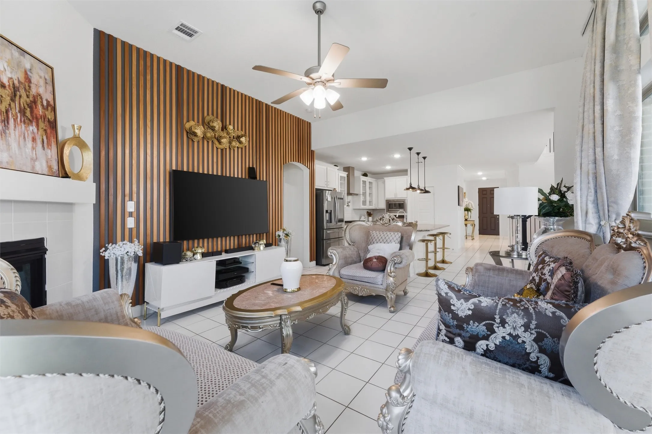 Living area featuring a distinctive slat wall accent, fireplace with white mantle, tile flooring, a ceiling fan, and recessed lighting