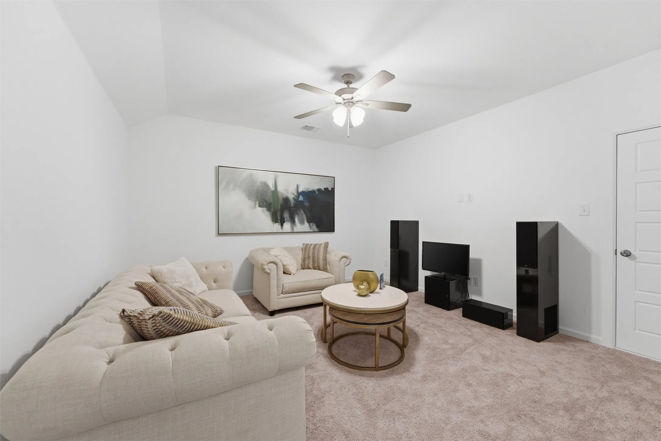 Spacious living area featuring neutral carpeting, white walls, and a ceiling fan with integrated lighting