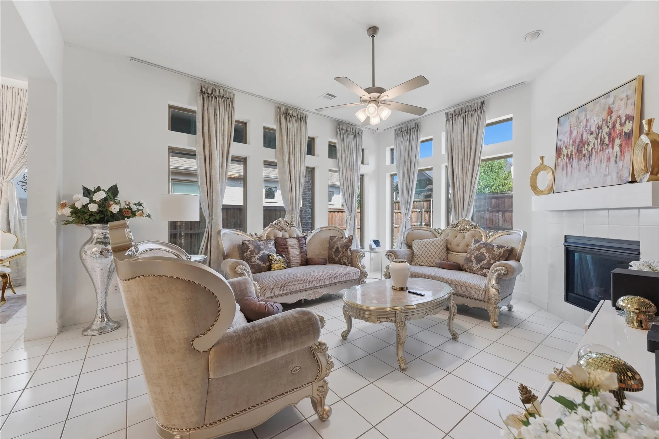 Spacious living area featuring high ceilings, white tile flooring, a fireplace with a white tile surround, a built-in mantel, and multiple large windows with vertical transoms