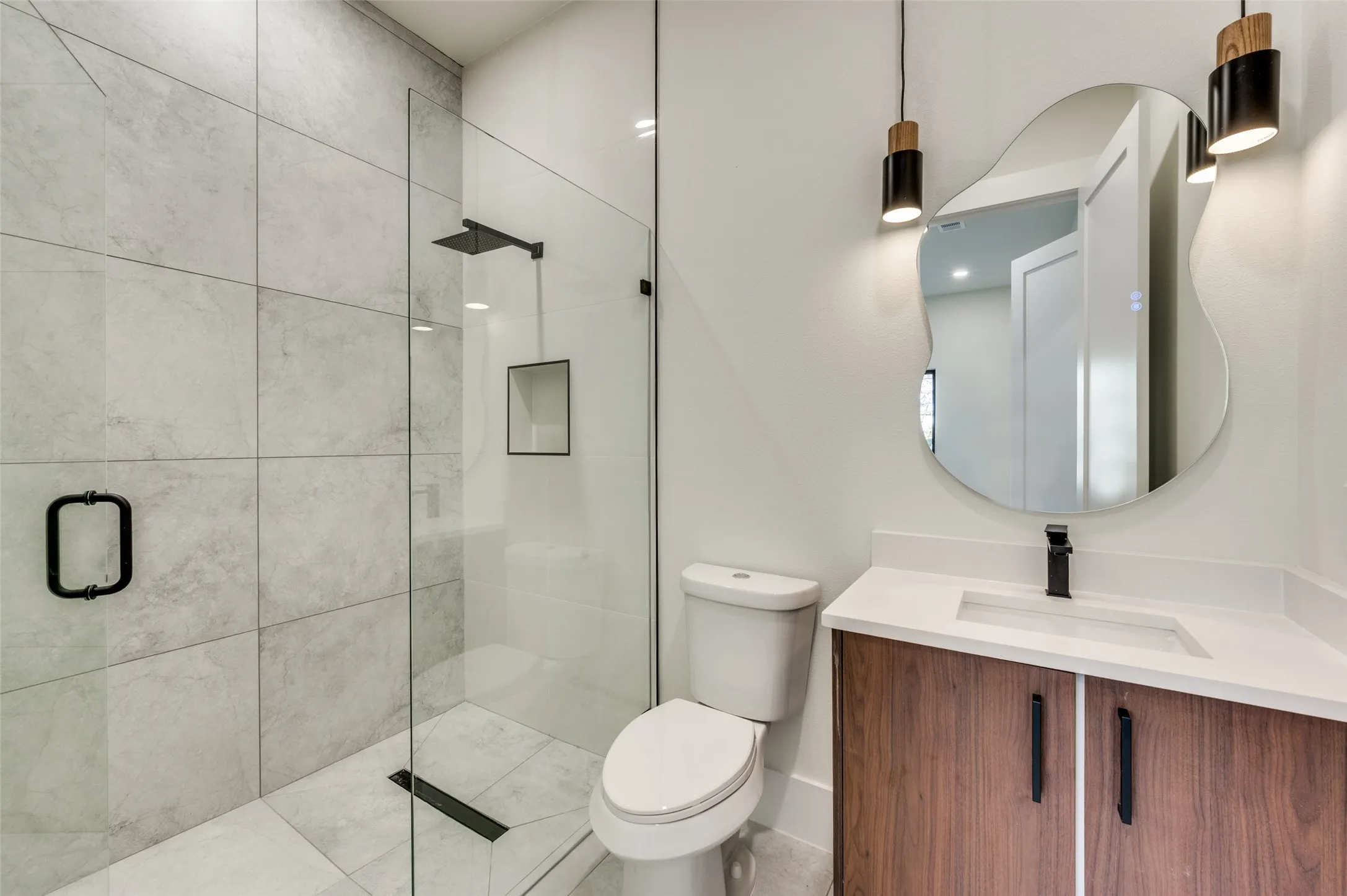 Contemporary bathroom featuring a glass-enclosed shower with large format tile, a built-in shower niche, and a matte black rain shower head