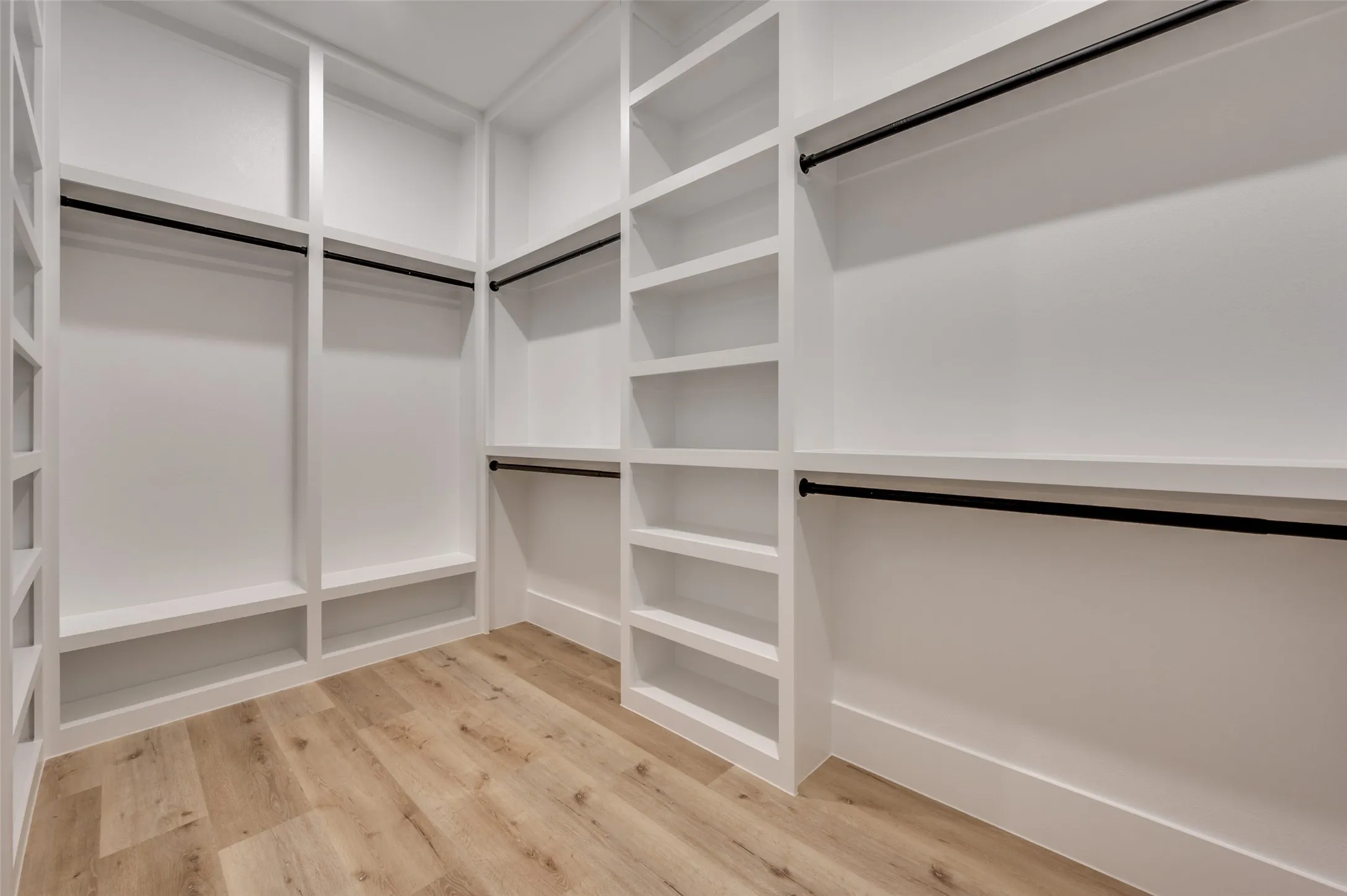 Built-in custom closet system featuring white cabinetry, multiple shelving units, garment rods, and light wood-finish flooring