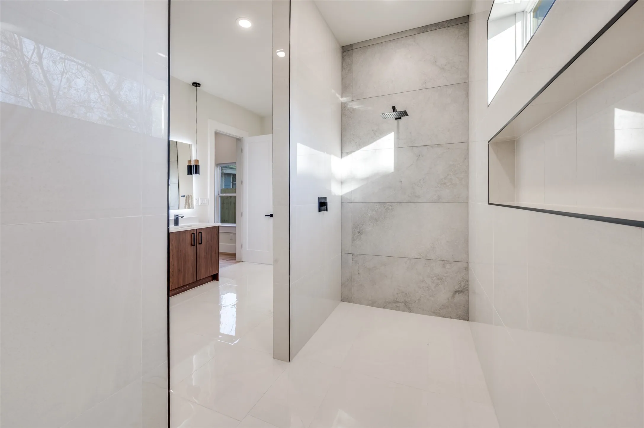 Open-concept shower featuring a rainfall showerhead, large format tile walls, and integrated shelving