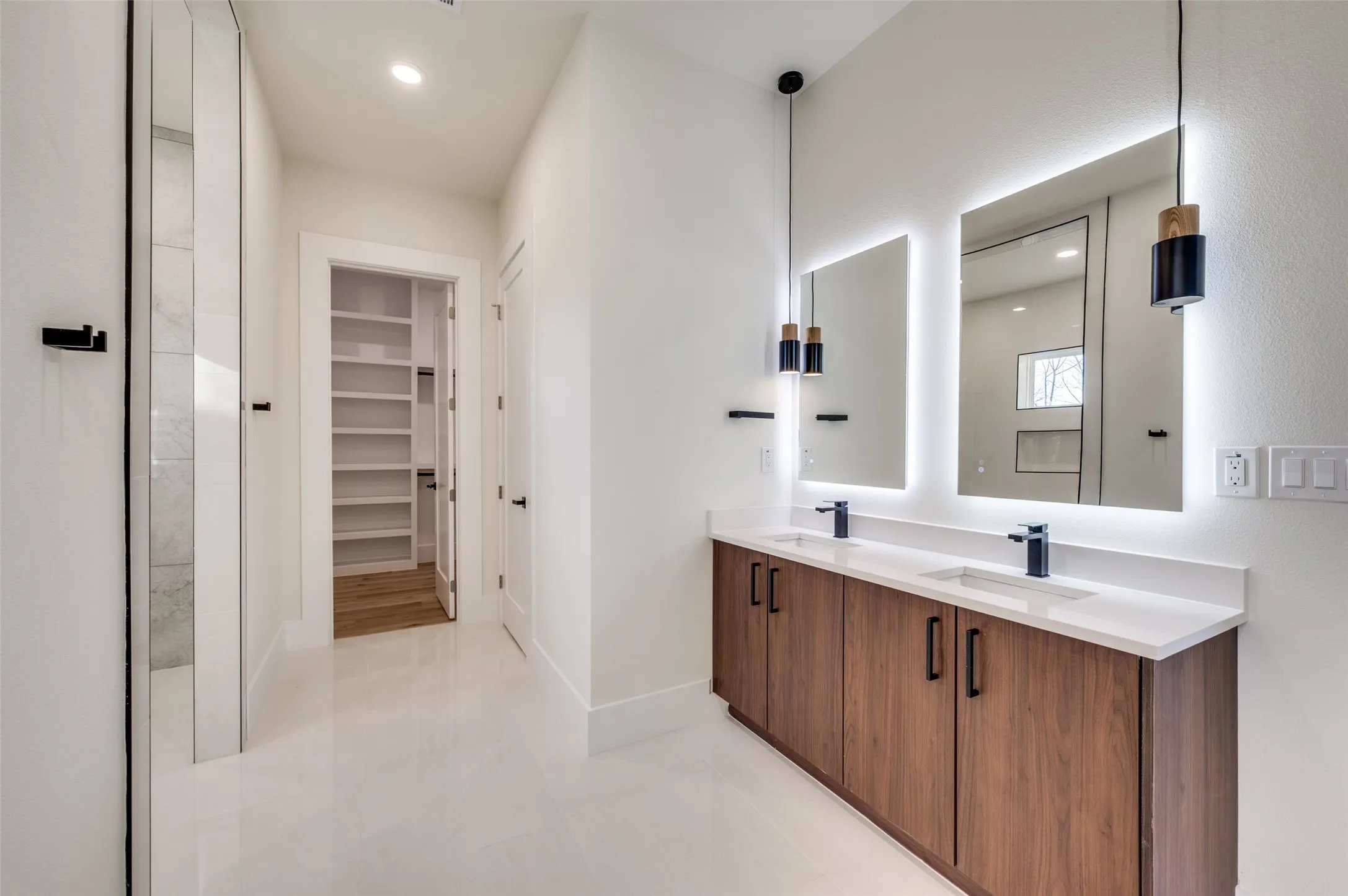 Dual vanity with wood-finish cabinetry, white countertops, and backlit mirrors