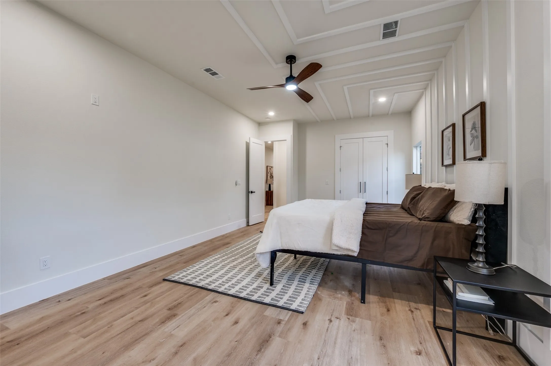 Spacious room featuring wood-finish flooring, a decorative tray ceiling with a ceiling fan, and white walls