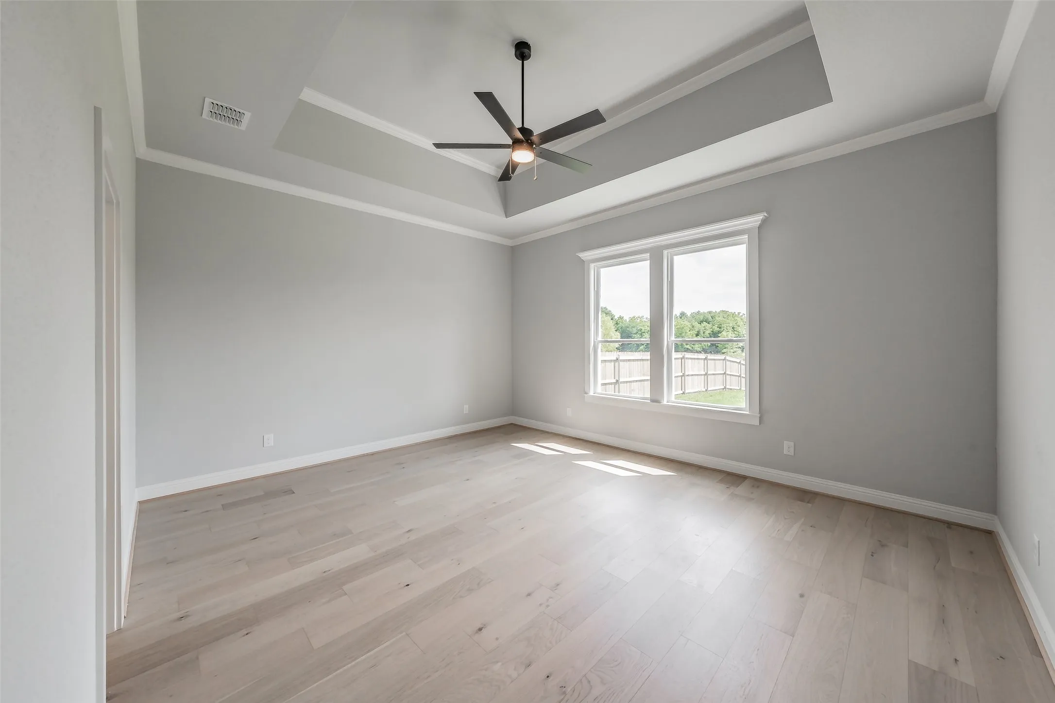 Huge primary bedroom features tray ceilings & a ceiling fan