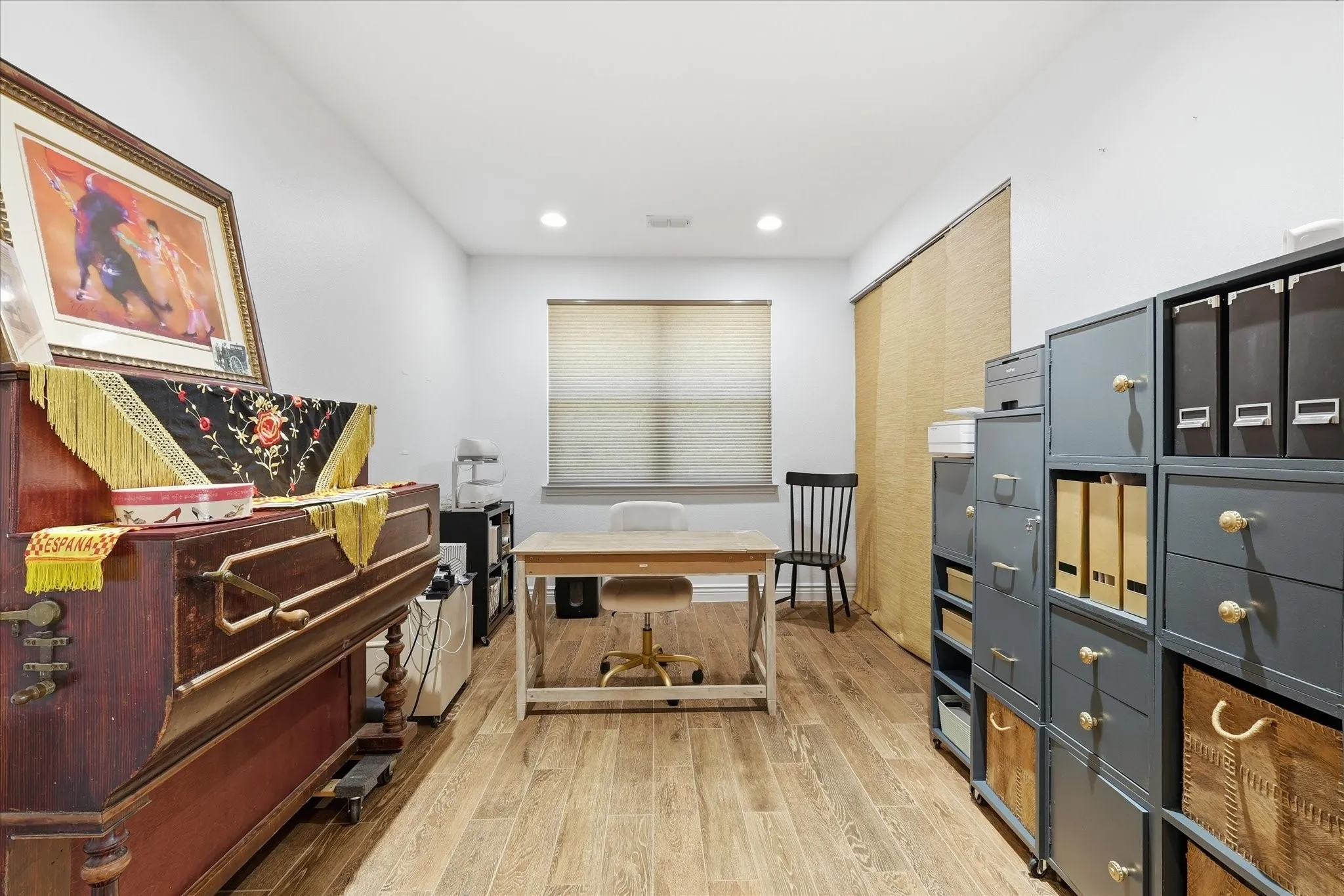Wood-finish flooring, recessed lighting, and a window with a woven shade create a versatile interior space