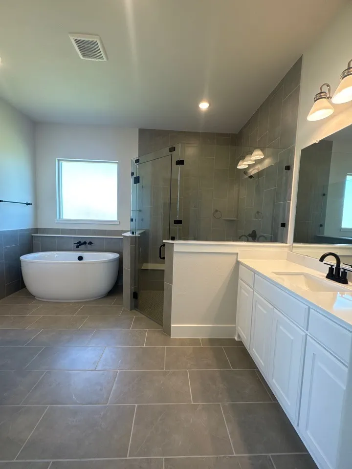 Freestanding soaking tub, frameless glass shower enclosure, dual vanity with white cabinetry, tile flooring, and recessed lighting