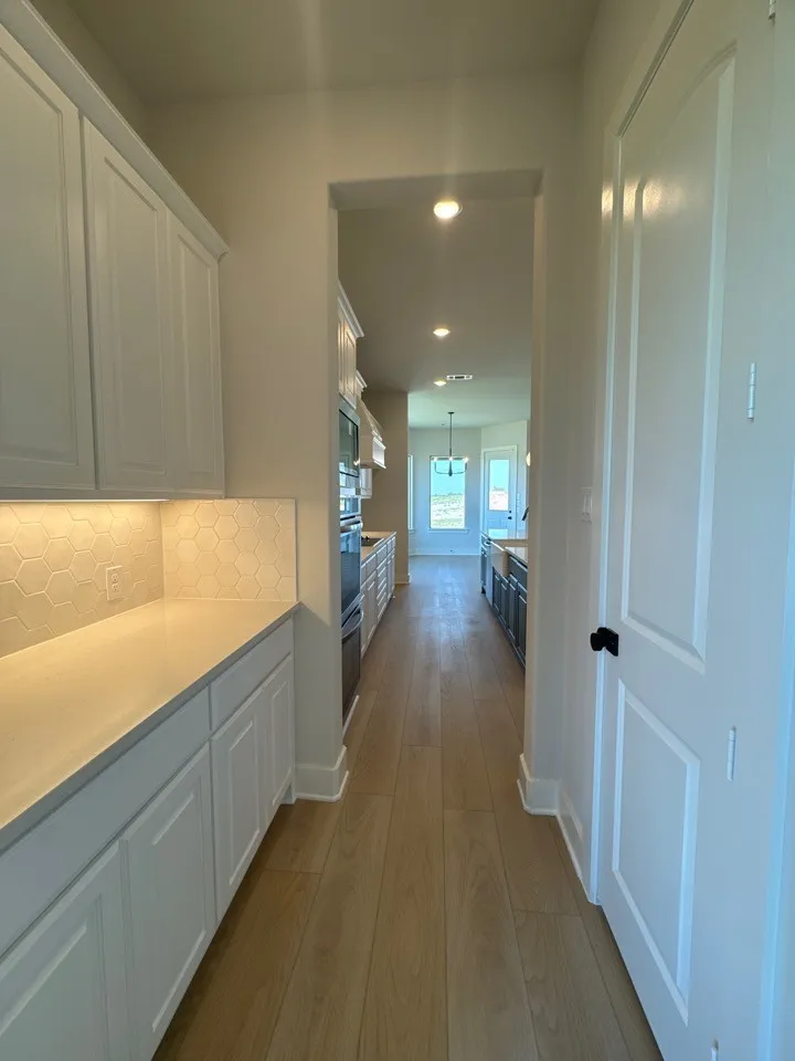 Galley-style kitchen with wood-finish flooring, recessed lighting, white shaker-style cabinetry, light-toned countertops, and hexagonal tile backsplash