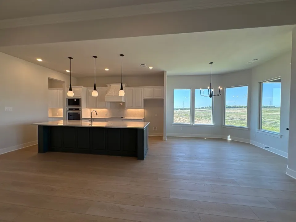 Kitchen island with pendant lighting, white cabinetry, integrated stainless steel appliances, and wood-finish flooring throughout