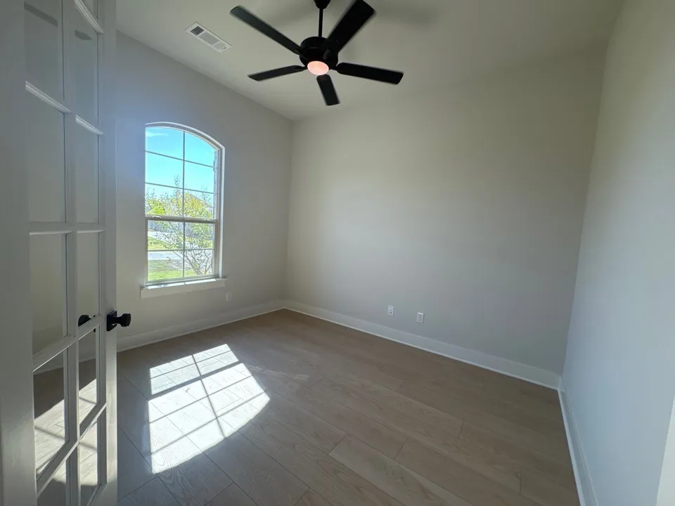 Arched window with gridded pane design, wood-finish flooring, ceiling fan, and French doors with matte black hardware