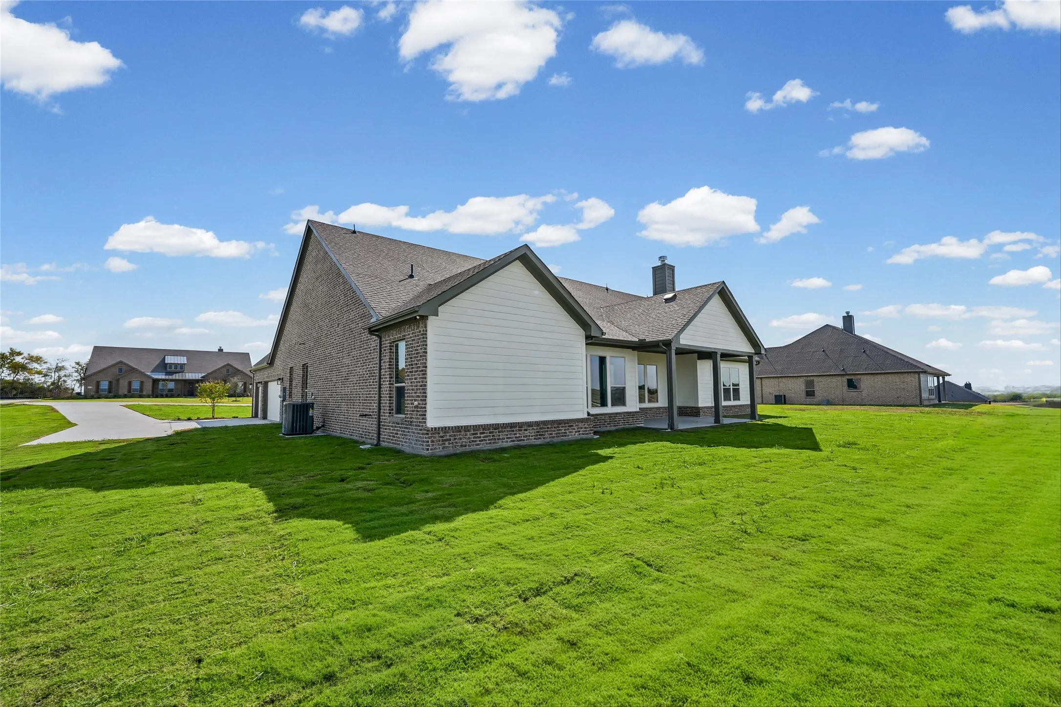 Brick and siding exterior with a covered patio and multiple windows overlooking a sprawling lawn