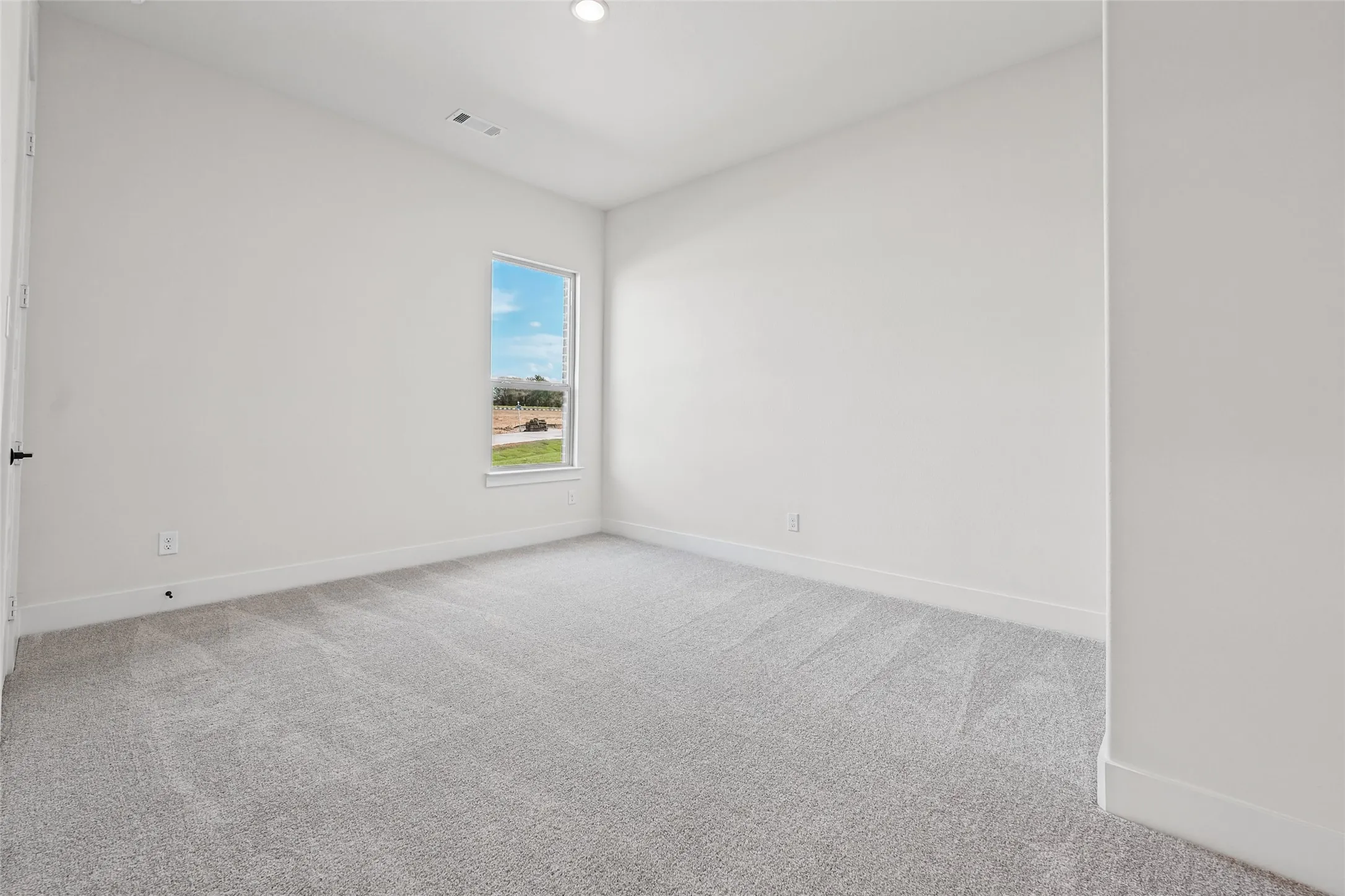 Expansive room featuring light gray carpeting, neutral wall finishes, and a single window offering exterior views