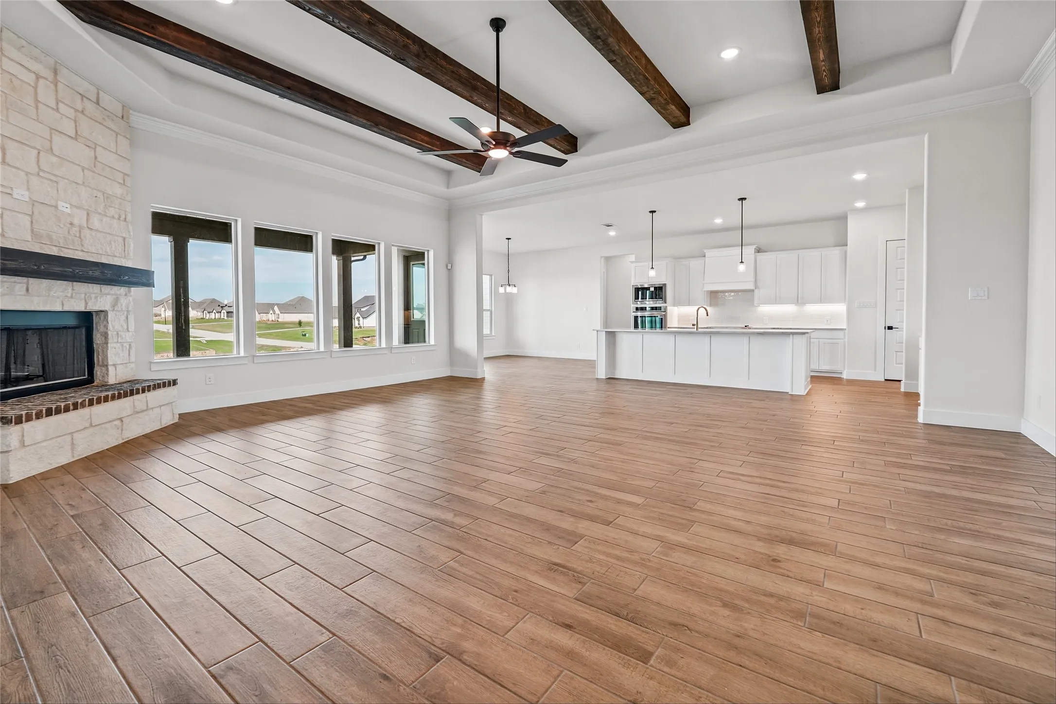 Spacious interior with wood-finish flooring, a stone-clad fireplace, exposed wood ceiling beams, and a modern kitchen with a large island and pendant lighting