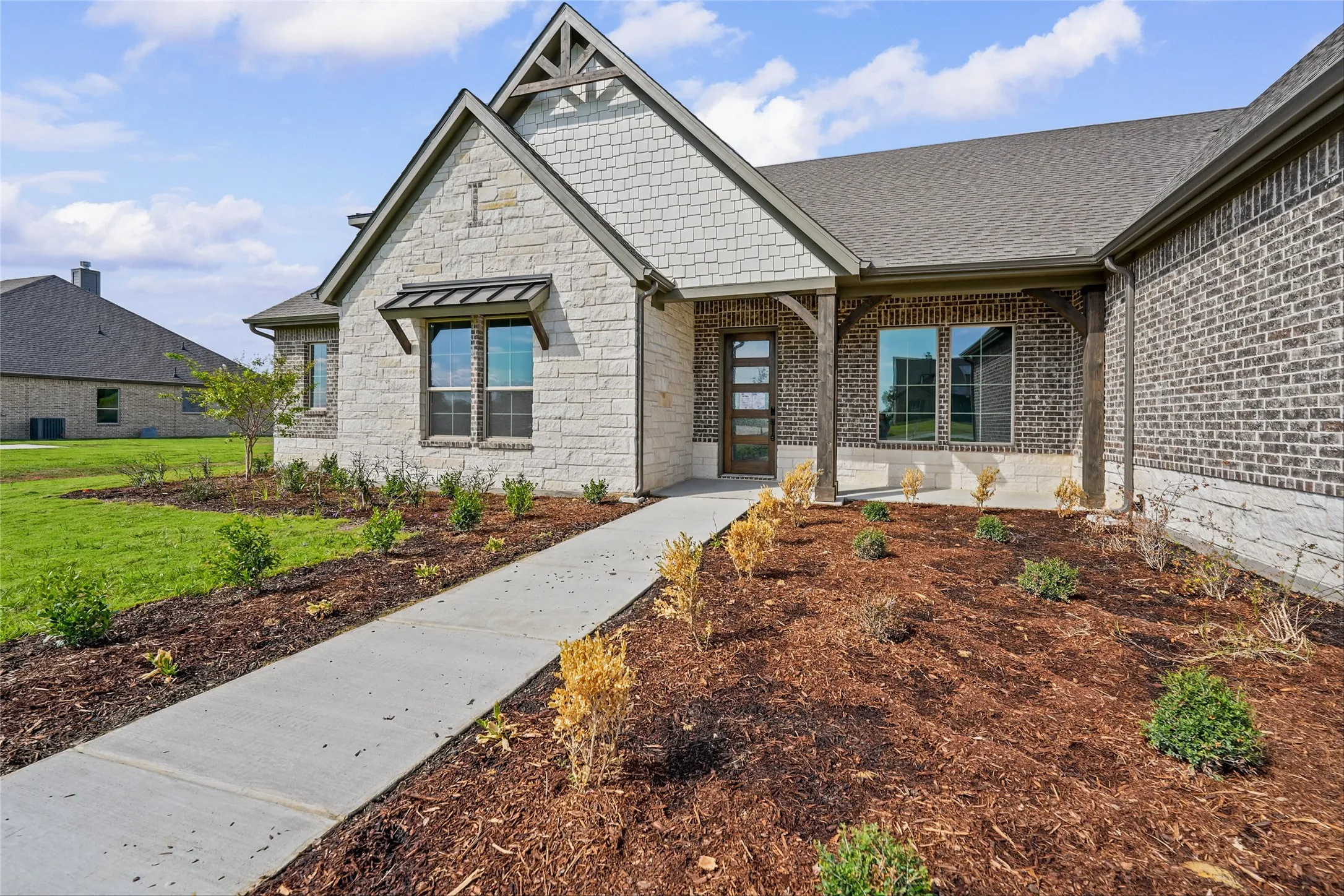 Stone and brick exterior with a prominent gable, covered entry with wood-finish columns, and an inviting walkway