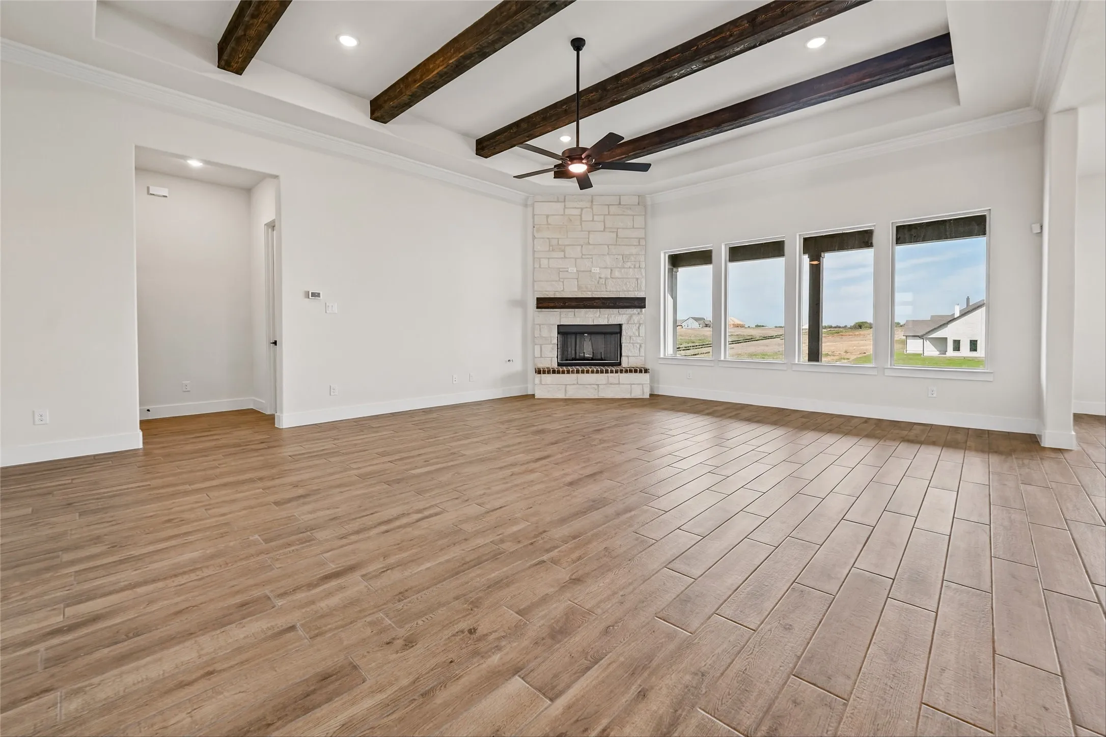 Wood-finish tile flooring throughout, a stone fireplace with a wood mantle, and a tray ceiling with exposed beams