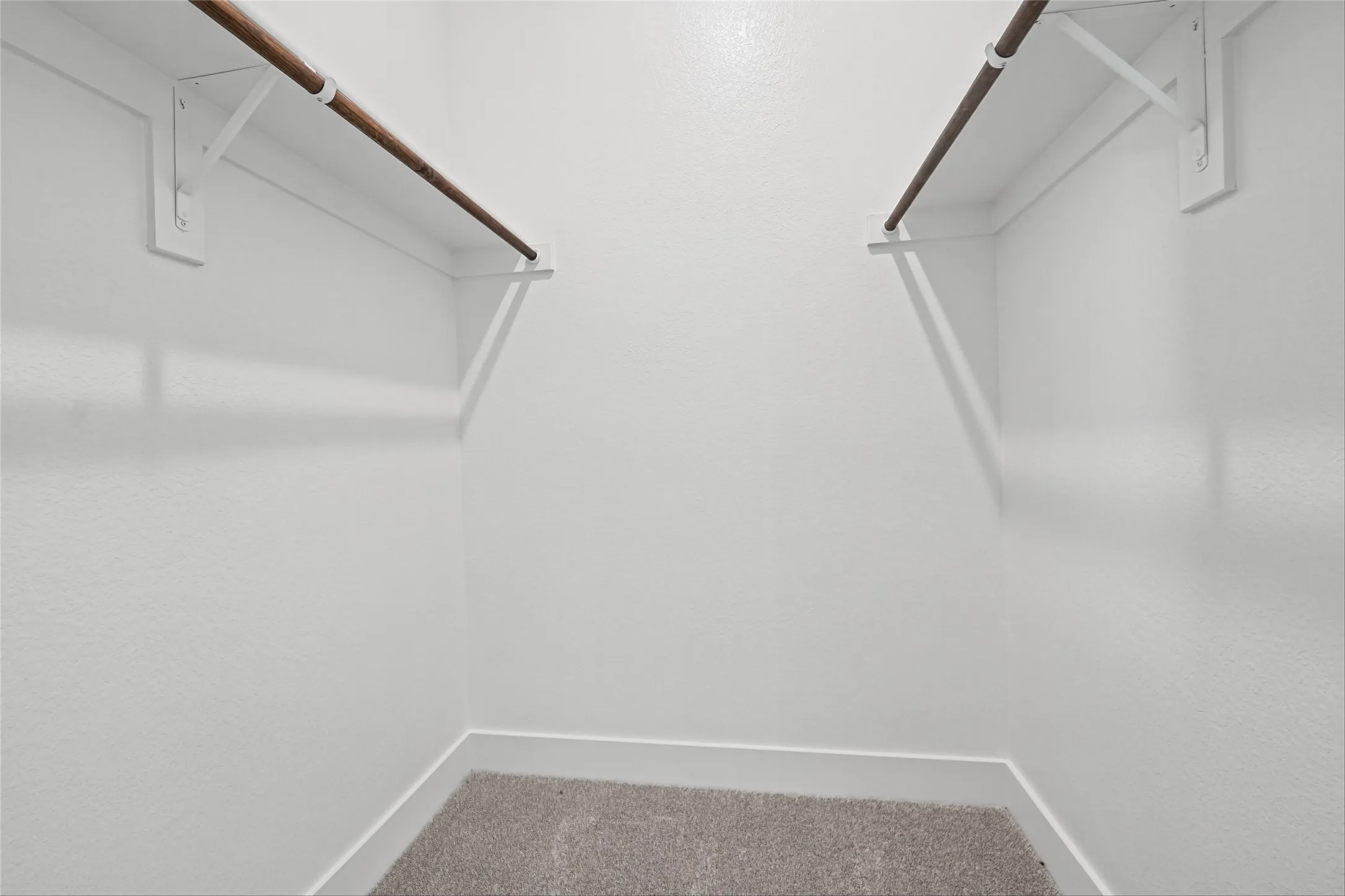White-painted walls with textured finish, light gray carpet flooring, and two wood-finish clothing rods with white supports