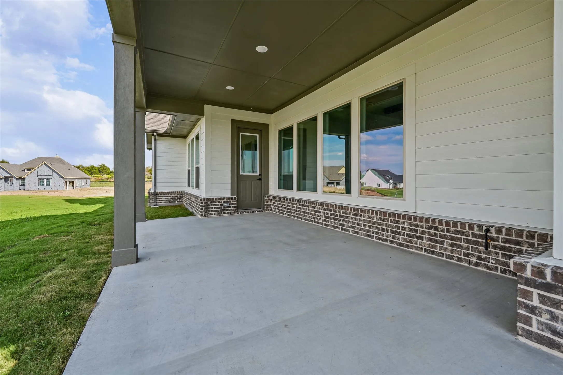 Covered patio with a concrete surface, featuring a white paneled exterior, a brick skirting, and recessed lighting