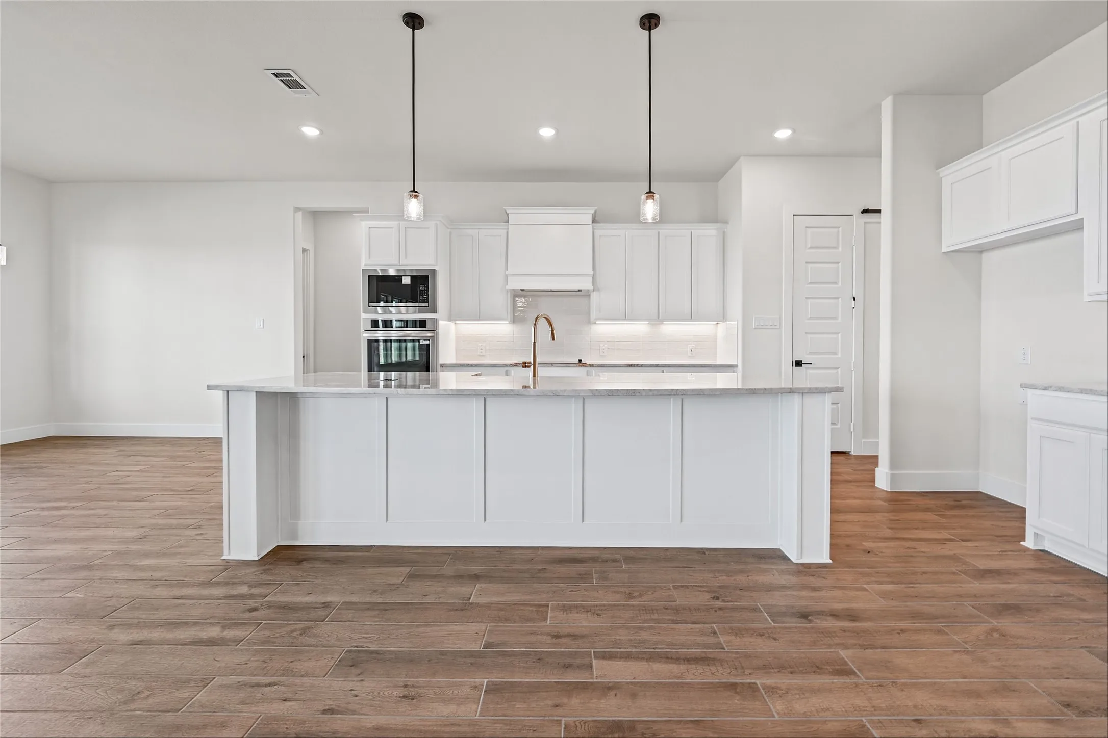 Kitchen featuring a large central island with a light-toned countertop, white cabinetry with integrated appliances, wood-finish flooring, and recessed ceiling lights
