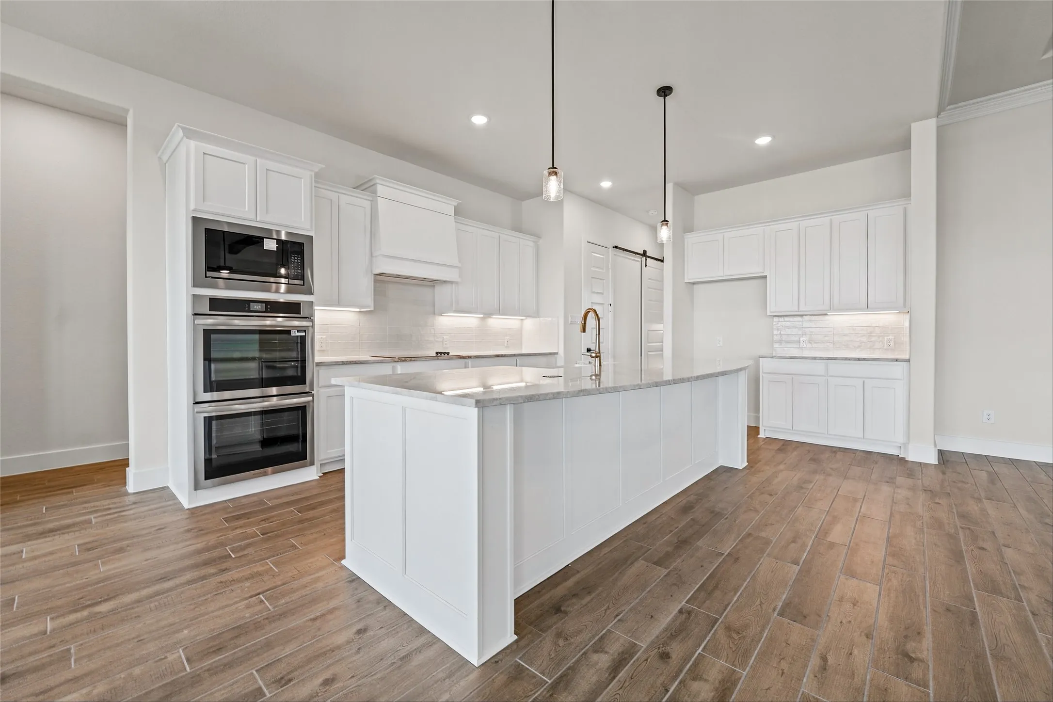 Spacious kitchen featuring white cabinetry, a large center island, stainless steel double ovens, and wood-finish flooring