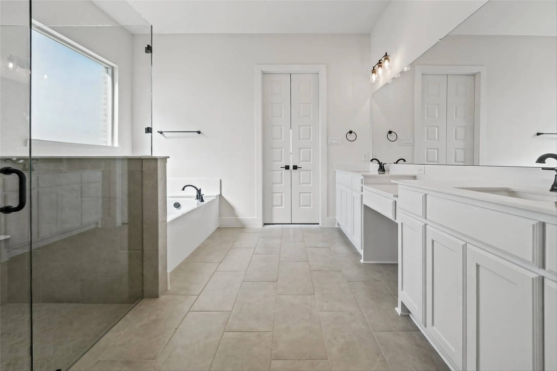 Spacious bathroom featuring a glass-enclosed shower, a separate soaking tub, dual vanities with white cabinetry and integrated sinks, and tiled flooring