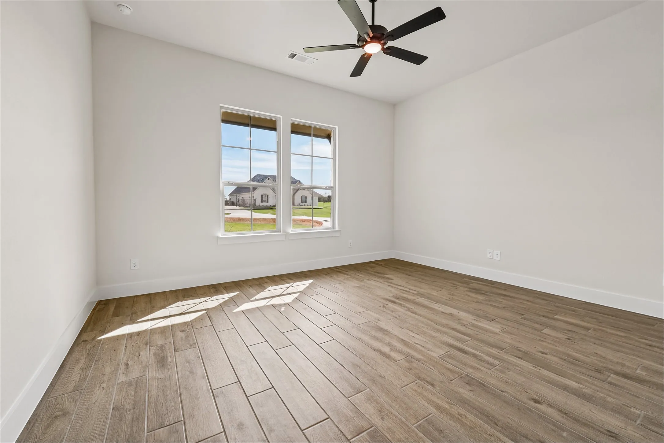 Vaulted ceiling with a ceiling fan, two large windows, wood-finish flooring, and crisp white walls