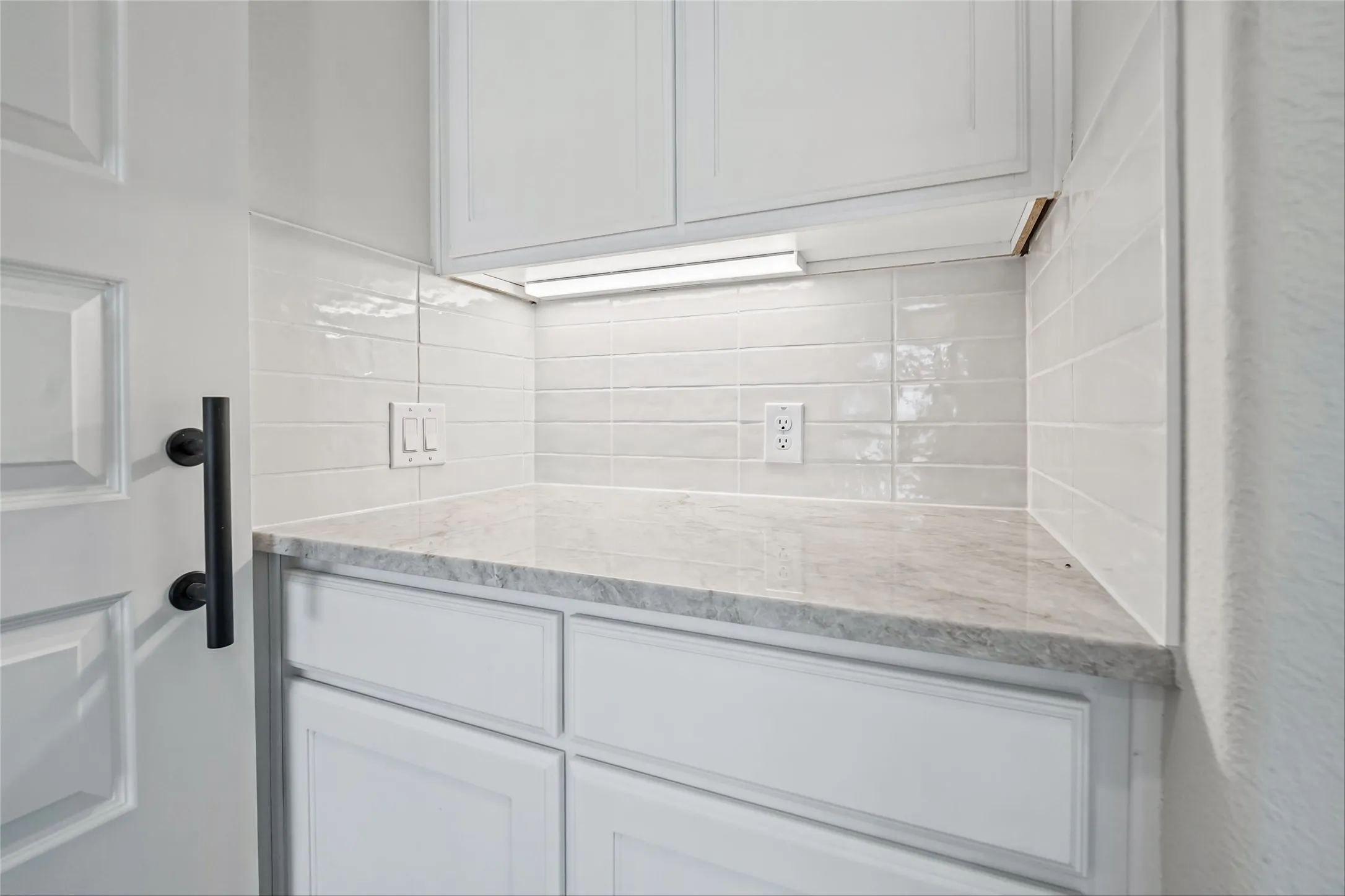 White cabinetry with paneled doors, light-toned countertop, and a white tile backsplash