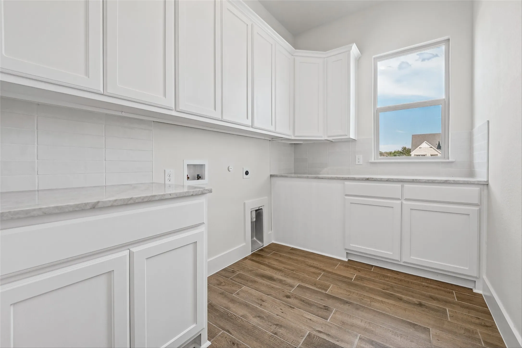 White shaker cabinetry with extensive storage, light-toned countertop, tile backsplash, wood-finish flooring, and a single pane window