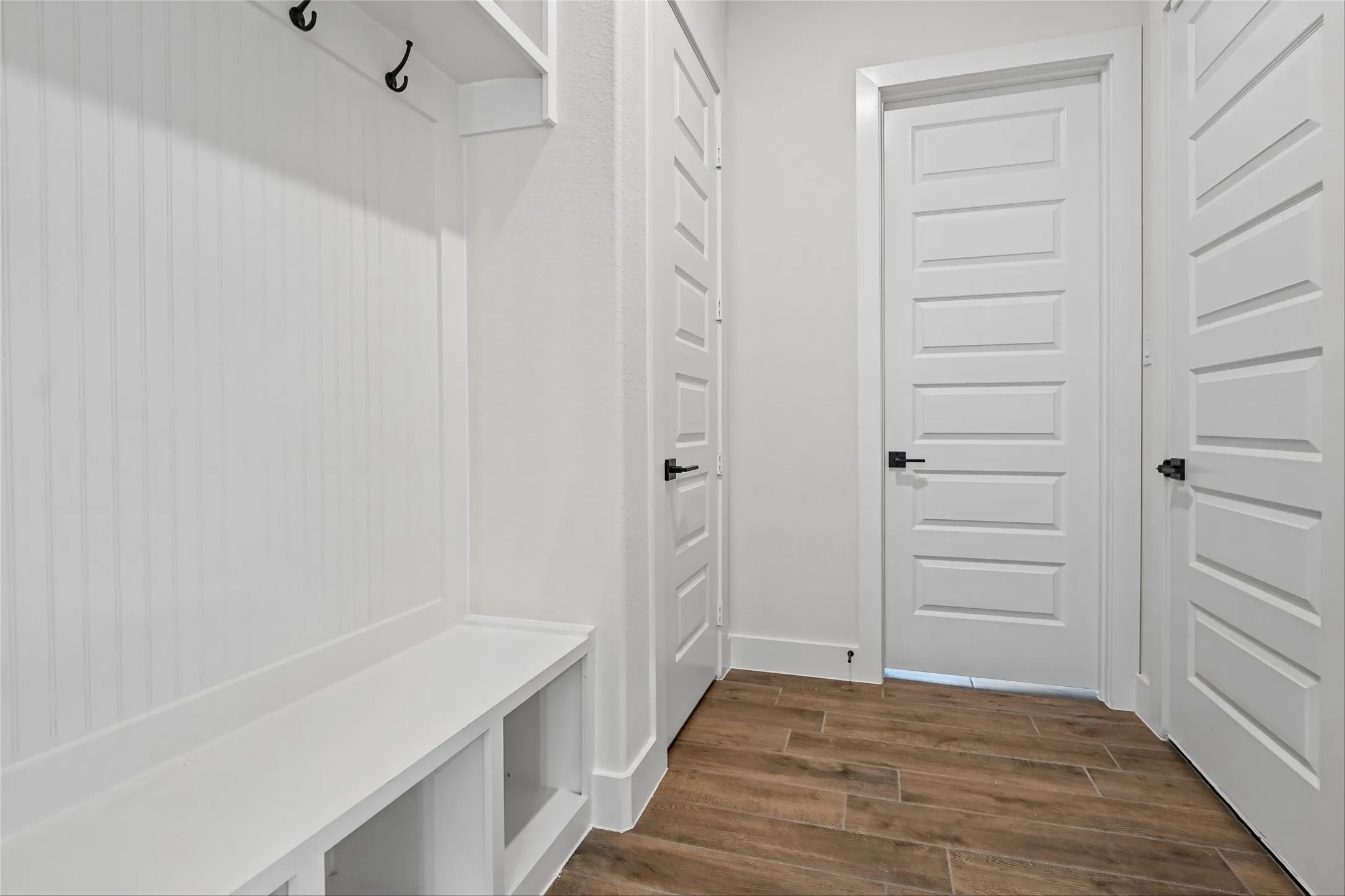 Built-in storage bench with open shelving, beadboard wall paneling, and black coat hooks