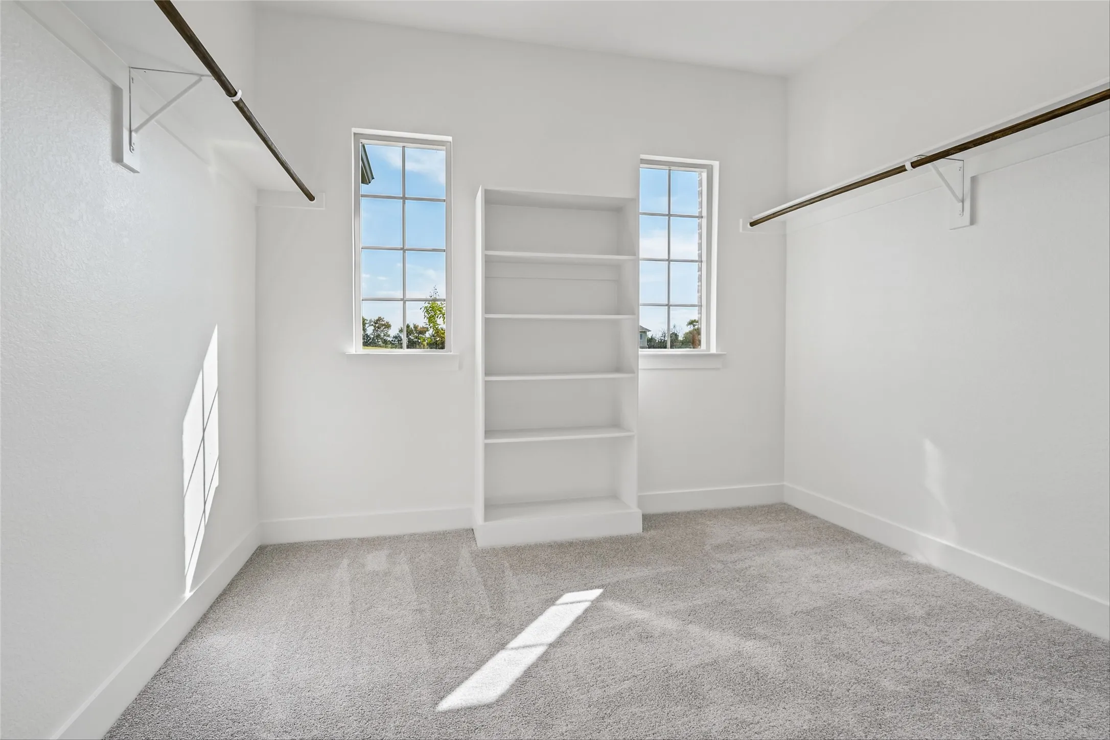 Carpeted room with two windows, a built-in shelving unit, and two clothing rods