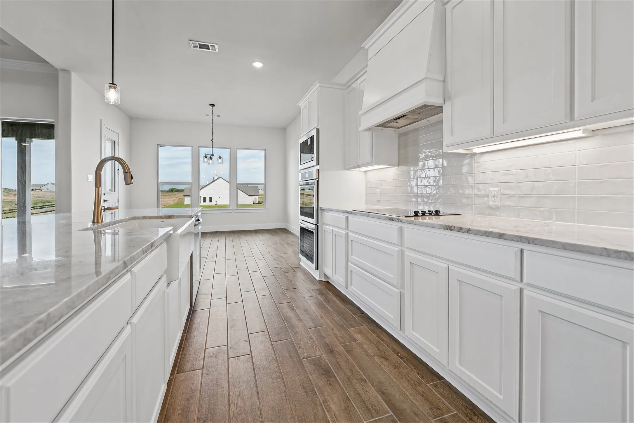 Contemporary kitchen featuring white cabinetry, light-toned countertops, wood-finish flooring, built-in double ovens, and a tile backsplash