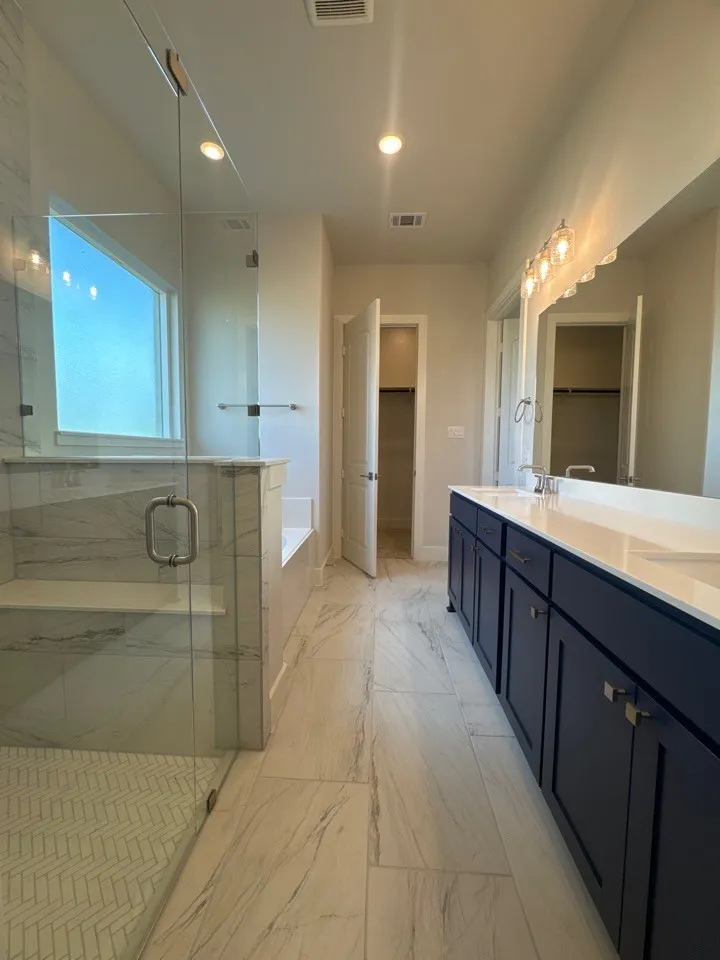 Spacious bathroom featuring a glass-enclosed shower with a built-in bench, a separate soaking tub, and a dual vanity with dark cabinetry and light countertops